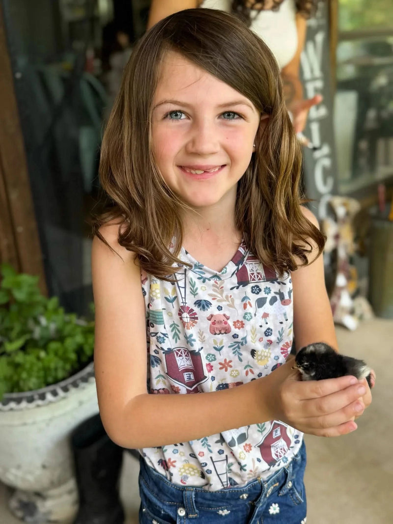 A young girl smiles, holding a chick, wearing a top with a barnyard print.