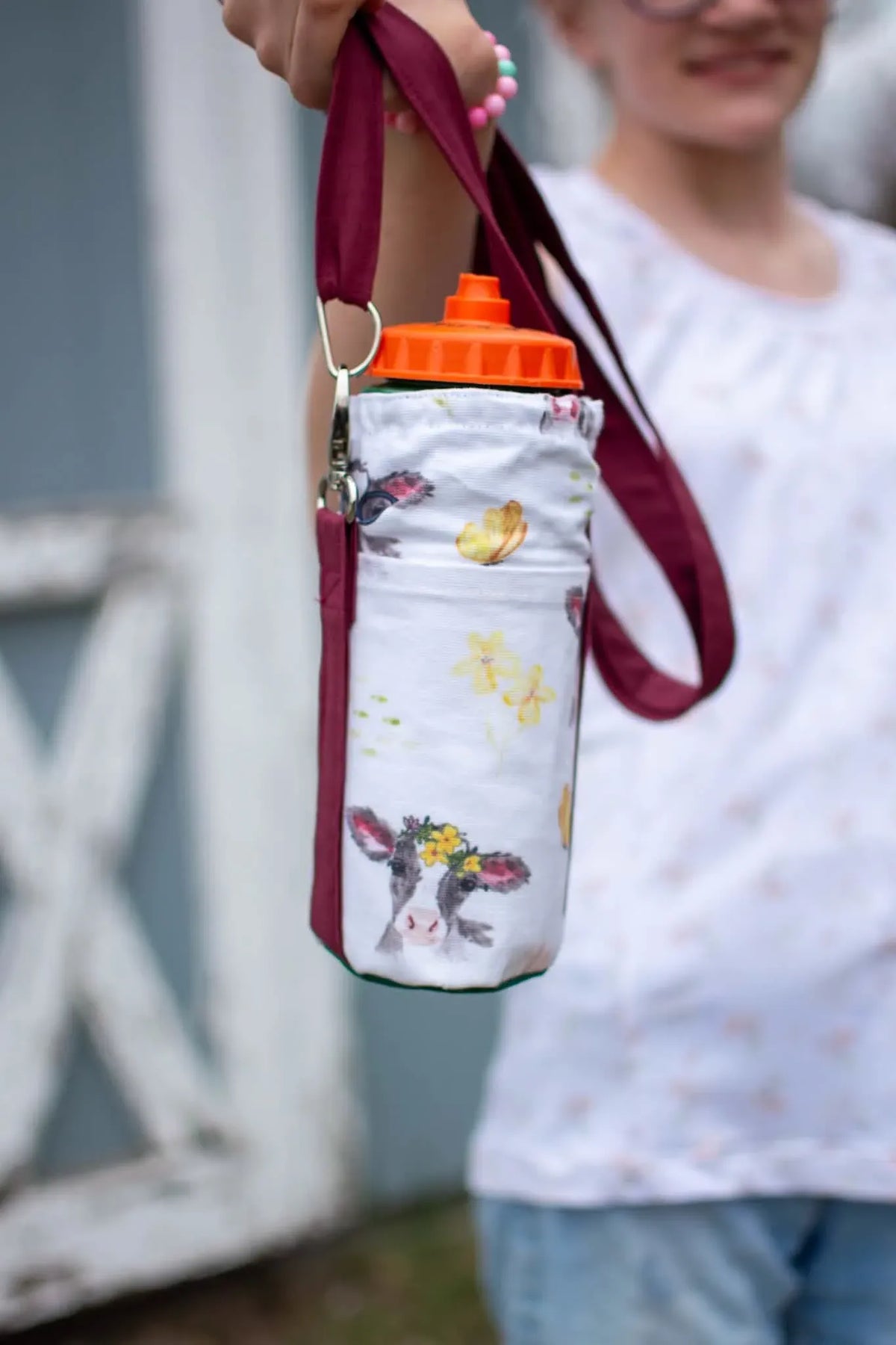 A water bottle holder with a cow and floral print, held by a person.