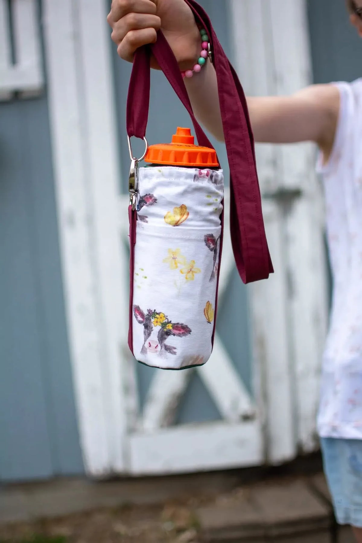 A person holds a water bottle in a white fabric holder with a calf and flower print.