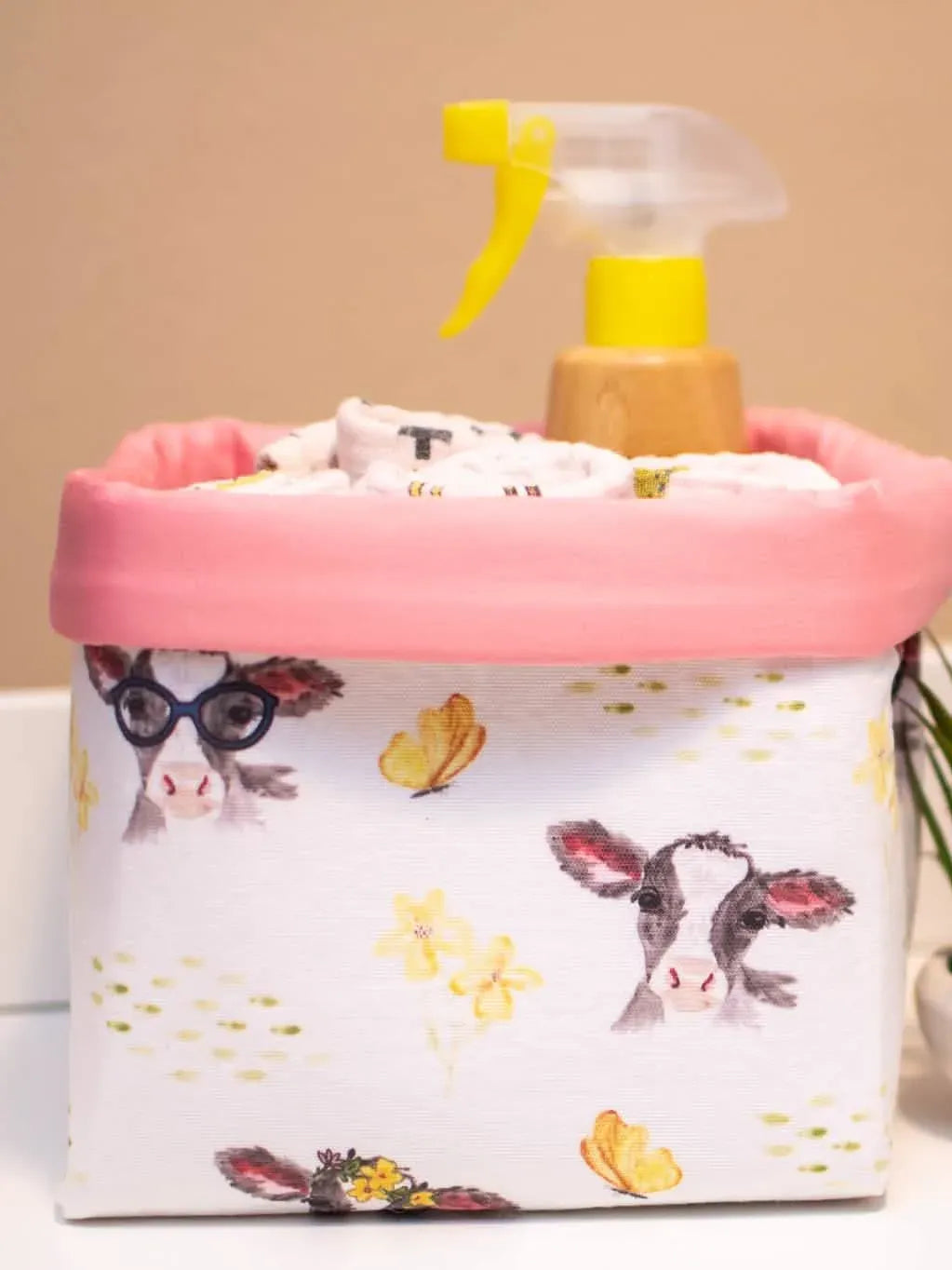 A fabric basket with a pink rim features a pattern of calves, butterflies, and yellow flowers.