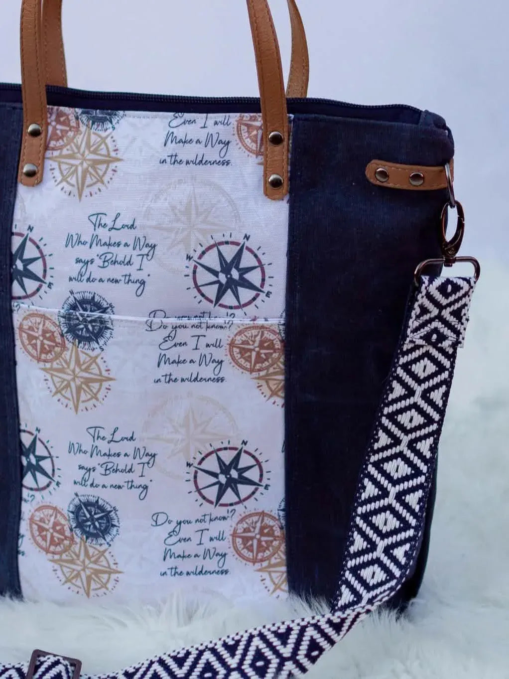A navy and white canvas tote bag with compass designs and scripture.