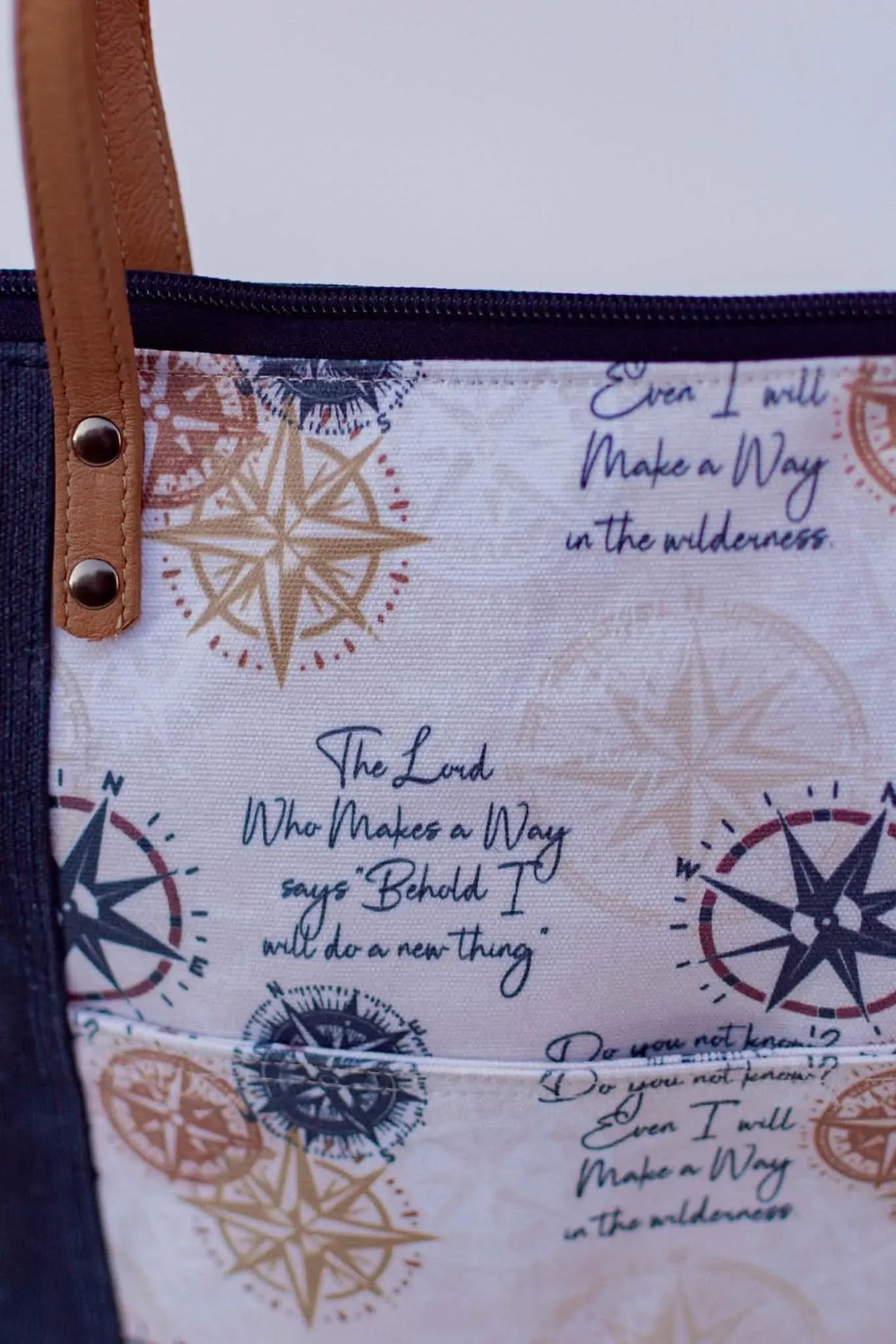 A fabric with compass designs and inspirational quotes, featuring a brown leather strap.
