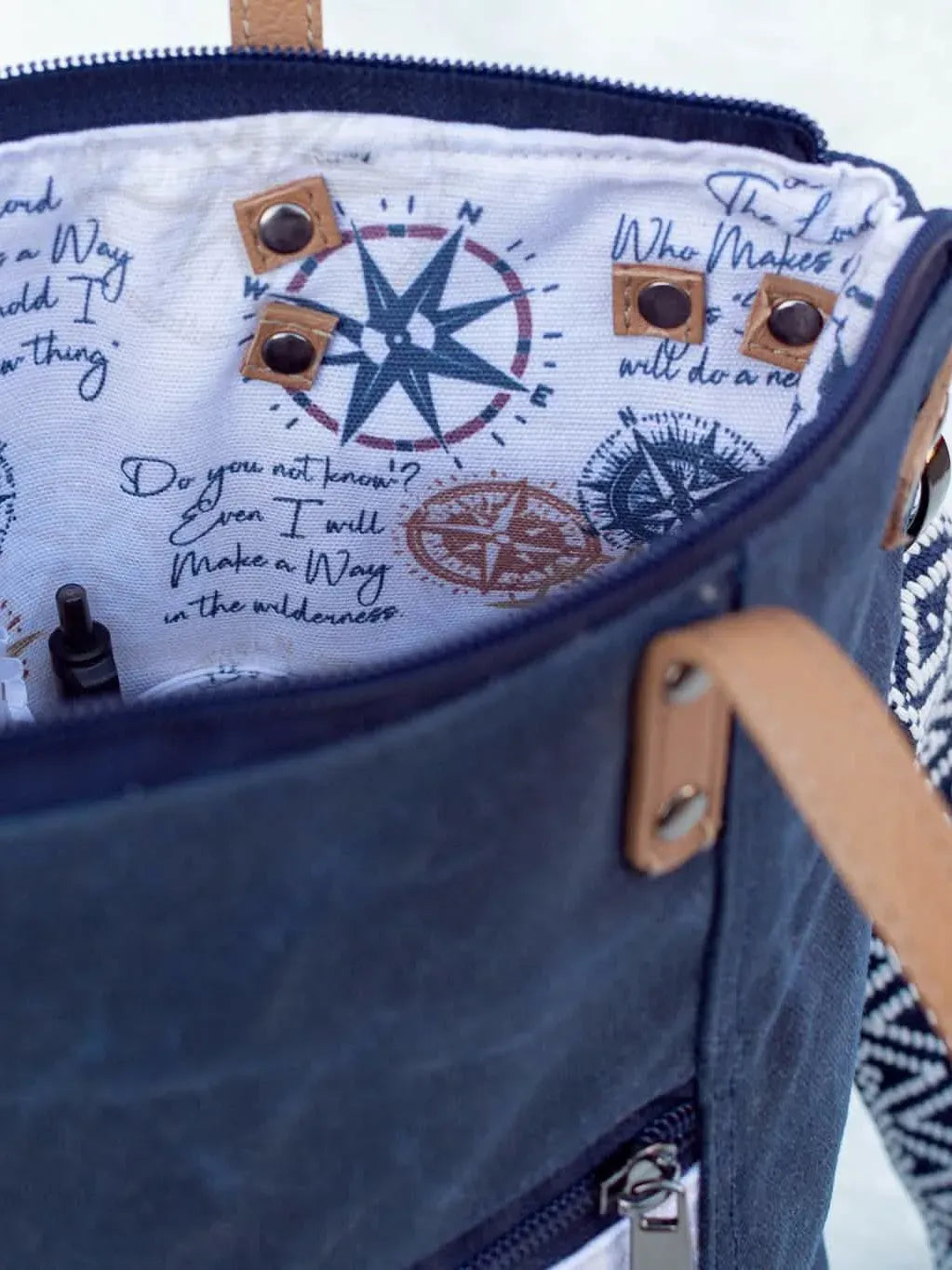 An open navy blue bag with a compass-themed lining and a notebook inside.