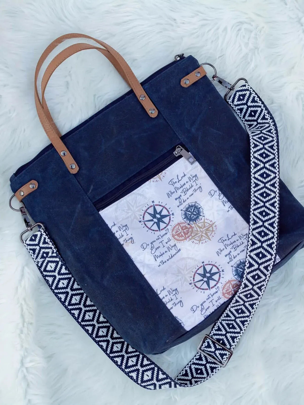 A navy blue canvas tote bag with brown leather handles and a compass-print pocket.