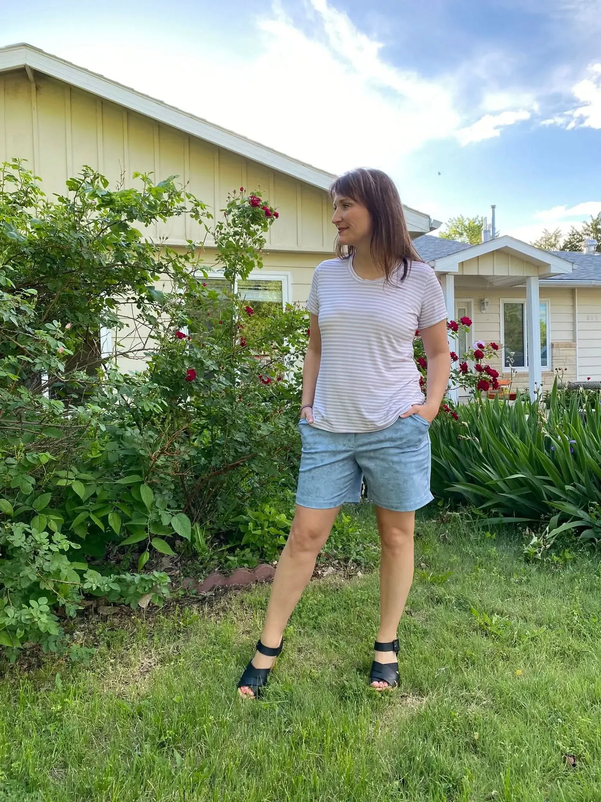 A woman wears a tan and white striped shirt with light blue shorts and black sandals.