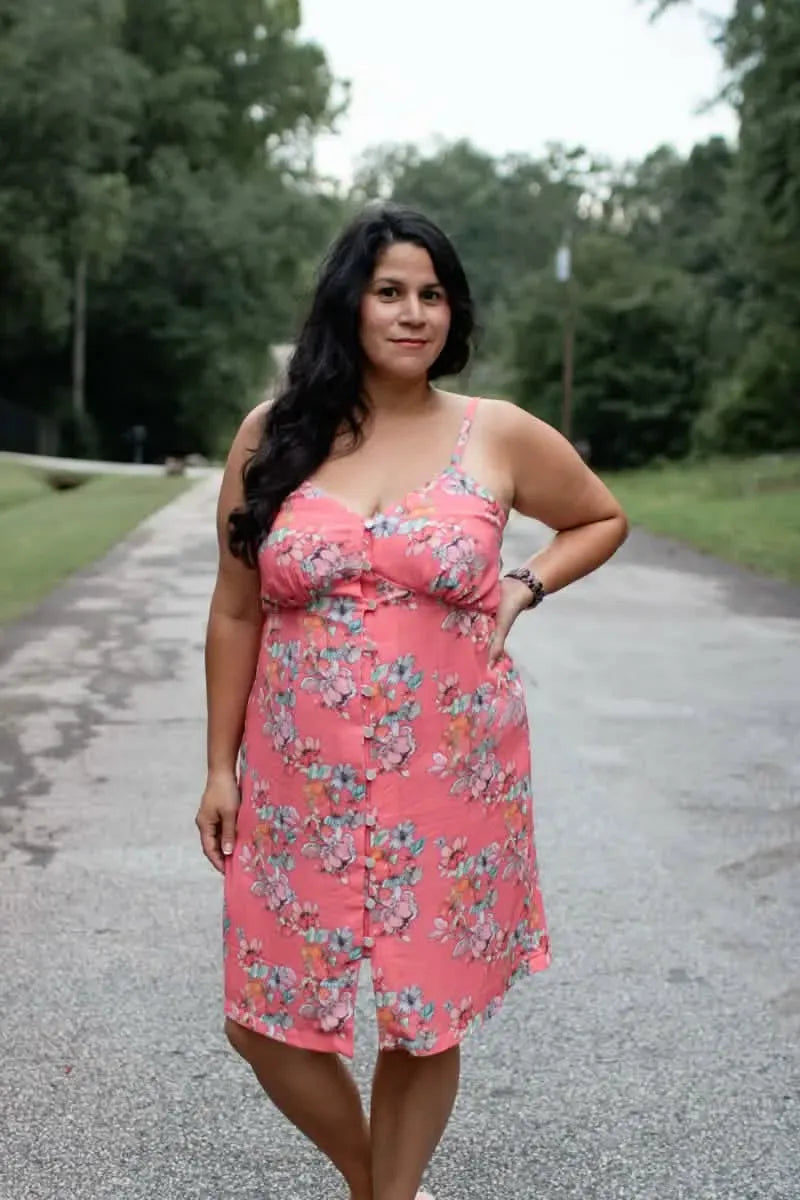 A woman in a floral pink dress stands on a paved road.