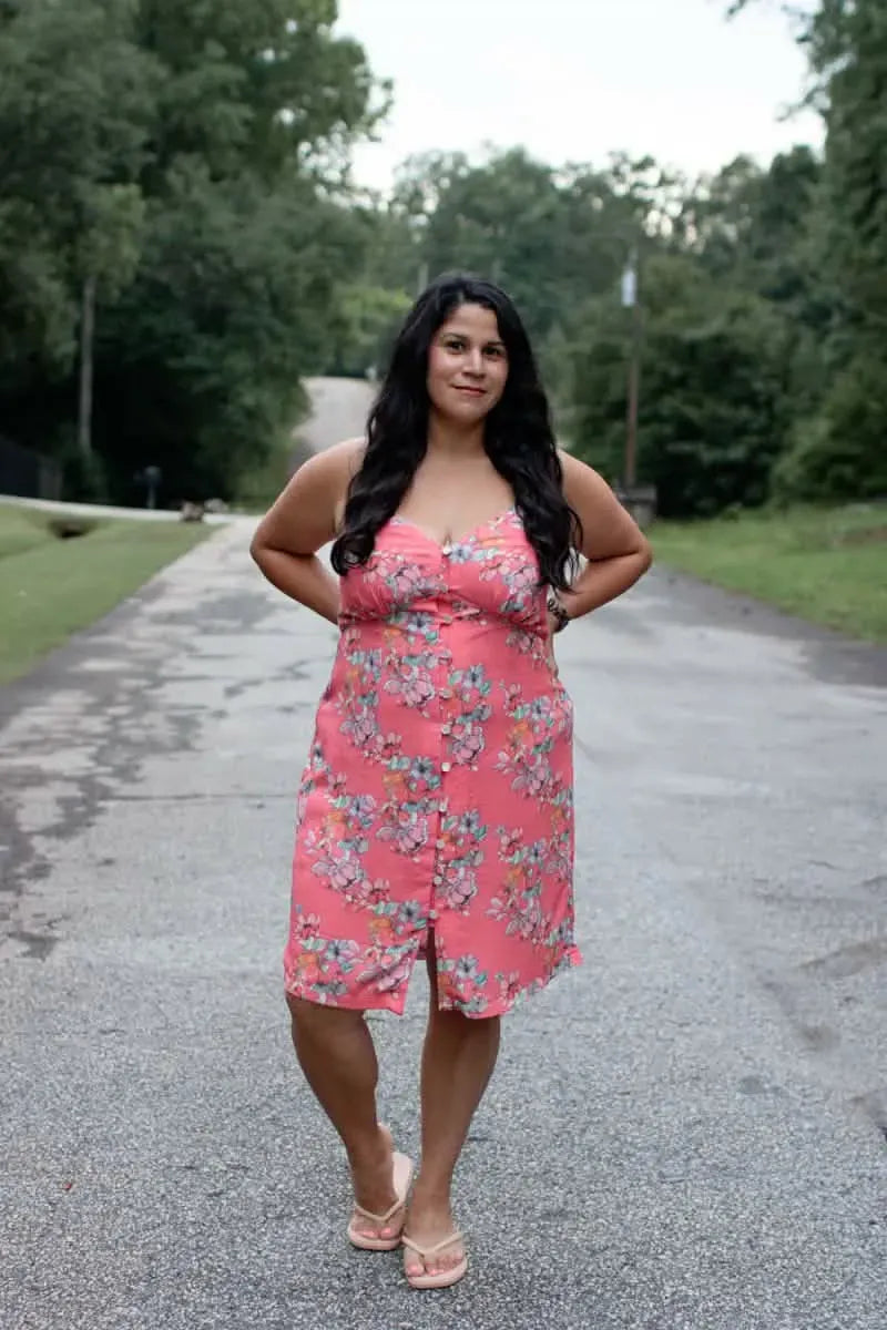 A woman in a floral pink button-down dress stands on a paved road.
