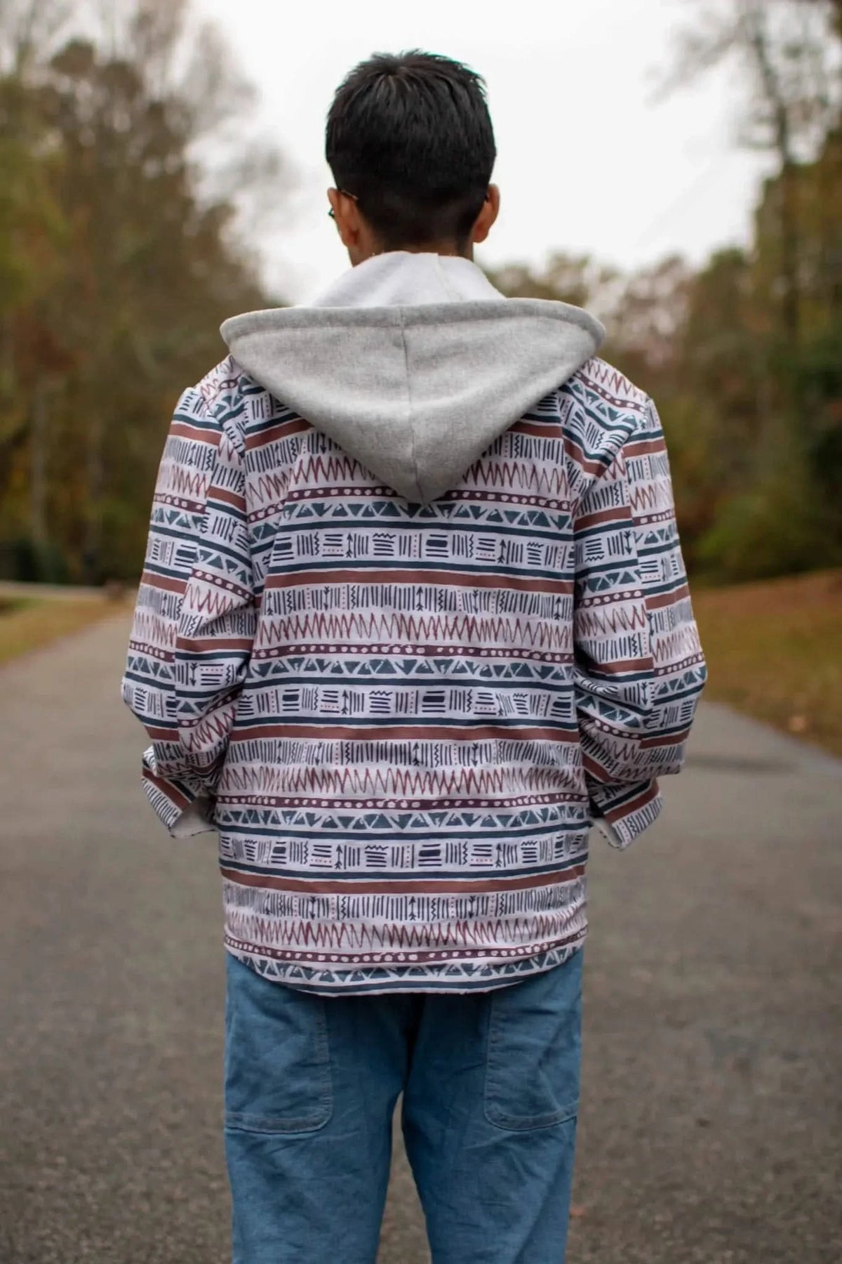 A person from behind wears a hooded shirt with a desert-inspired pattern and blue pants.