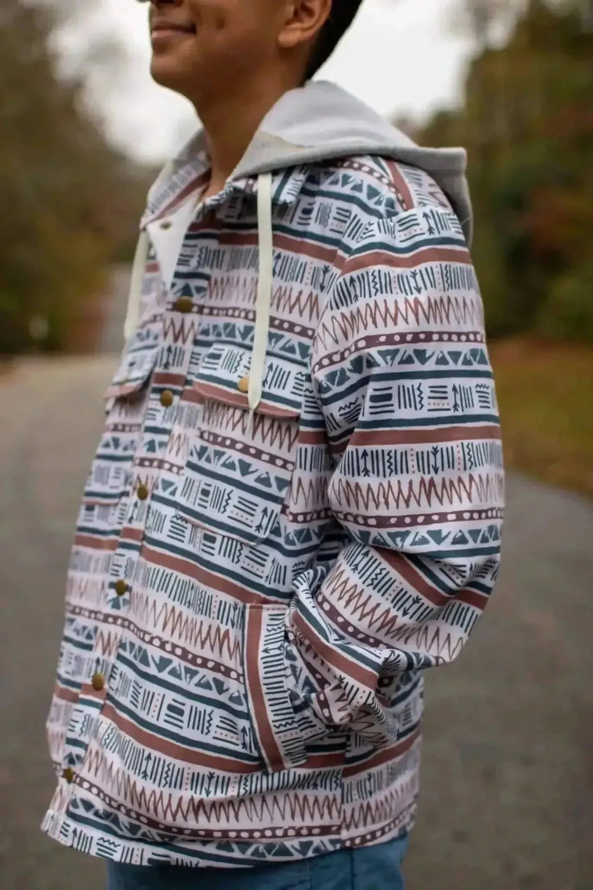 Man wearing a gray-hooded jacket with white, navy, and rust geometric patterns outdoors.