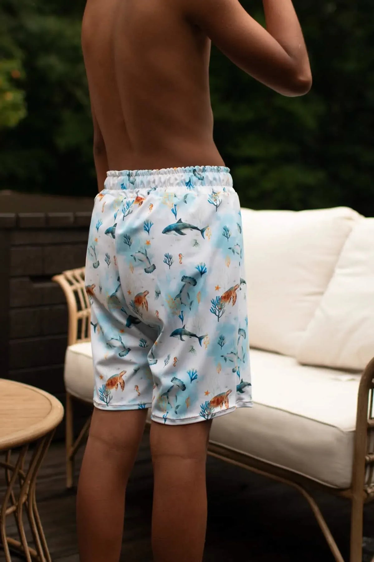 A person from behind wearing blue swim shorts with an underwater sea life pattern.