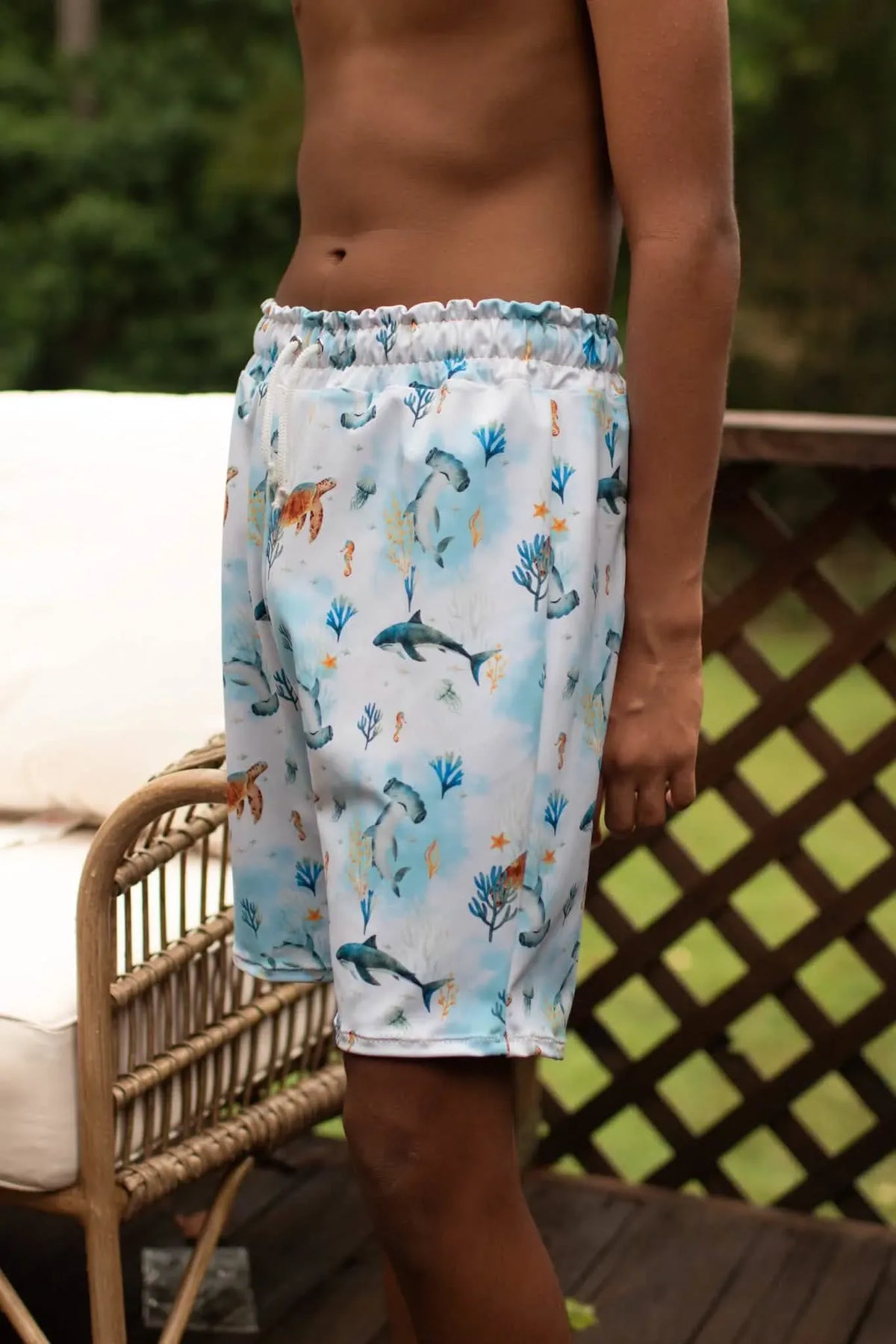 A person models swim shorts with an "Under The Sea" pattern.