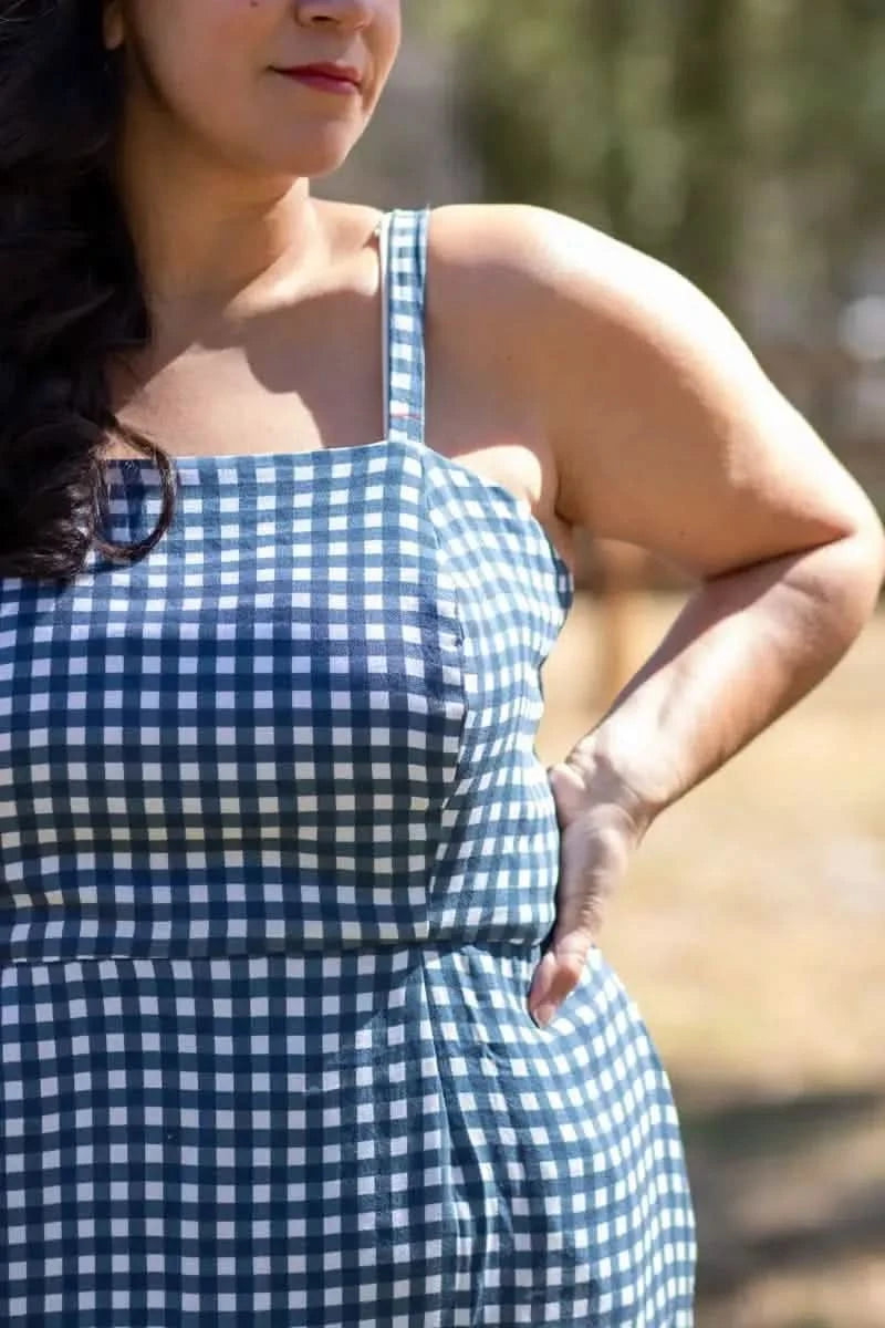 A woman wears a navy and white gingham dress with thin straps.