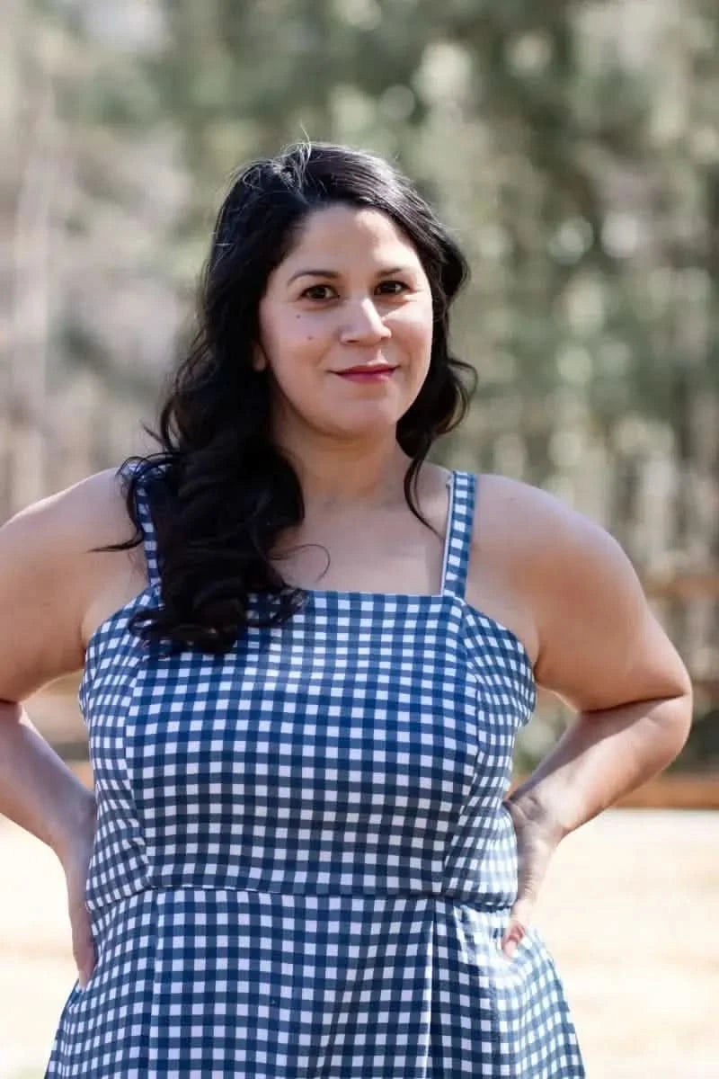 A woman in a navy gingham dress with her hands on her hips.