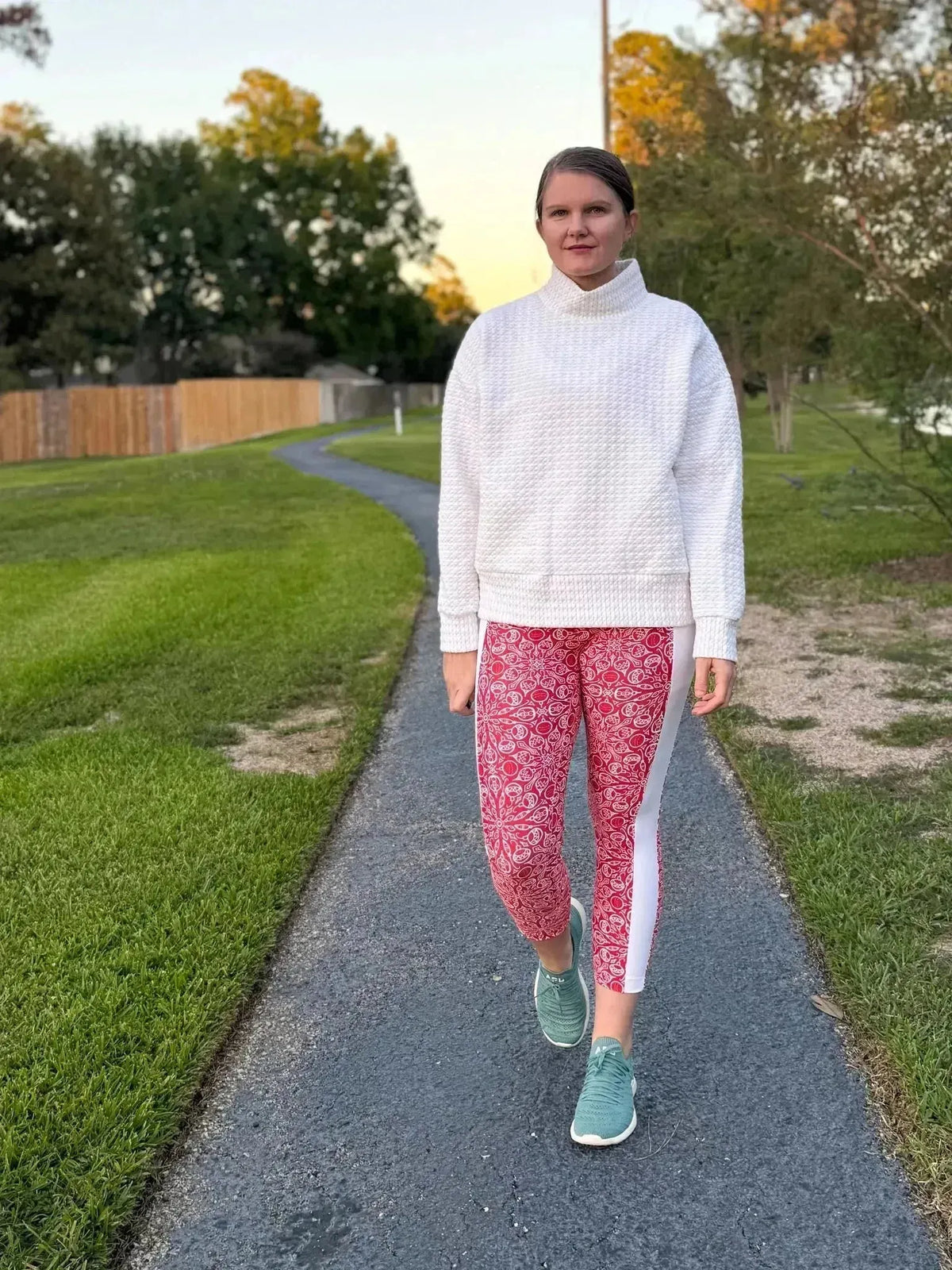 Woman wearing white sweatshirt and red Christmas print leggings with white stripes, walking outdoors.