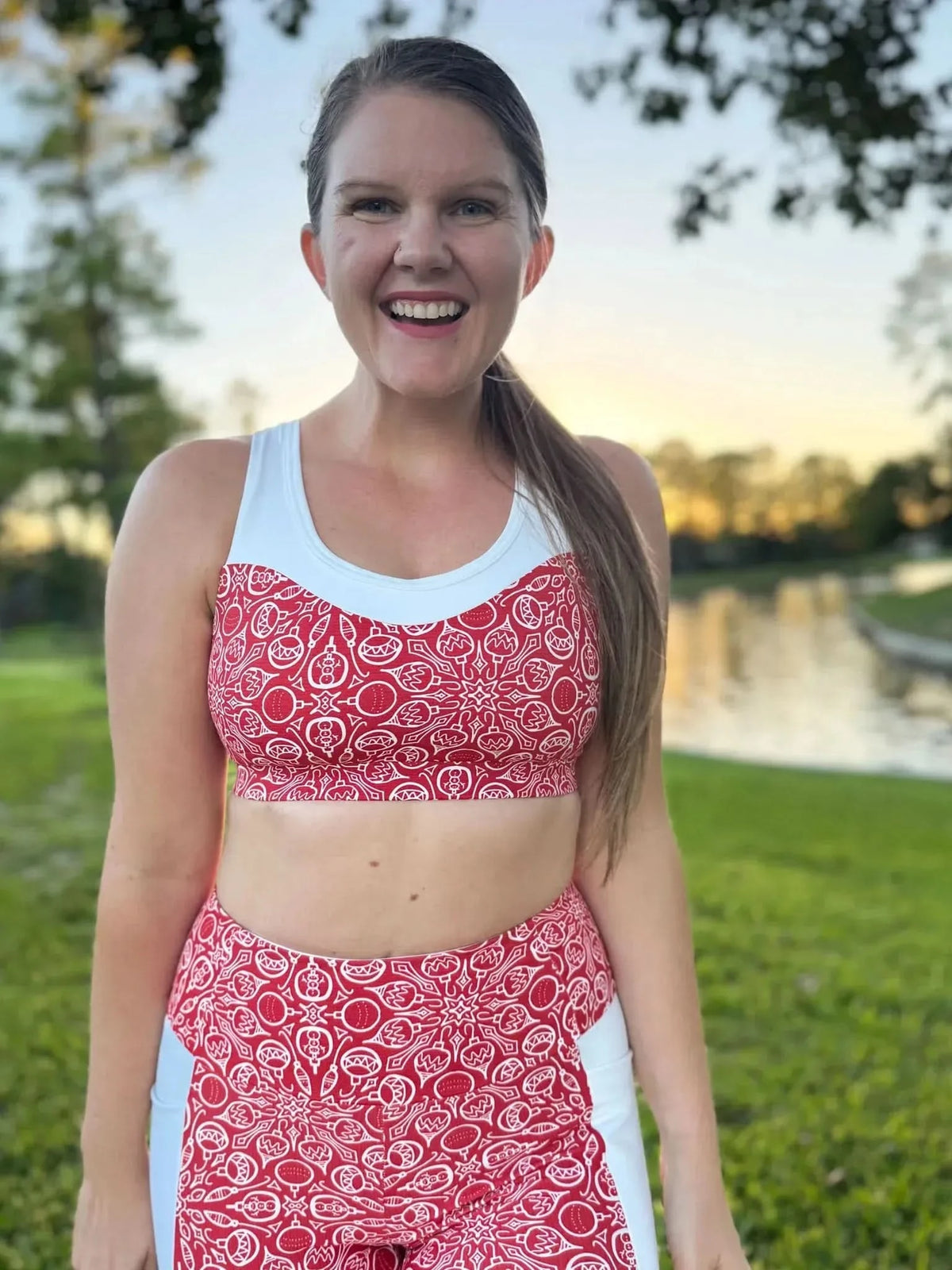 A woman smiles wearing a red and white Christmas sweater patterned sports bra and leggings.