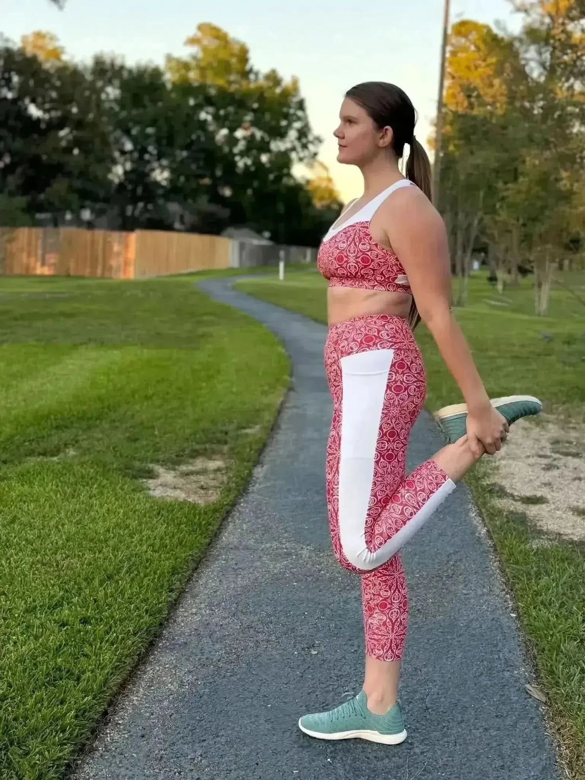 Woman wearing red holiday print leggings and sports bra, stretching outdoors.