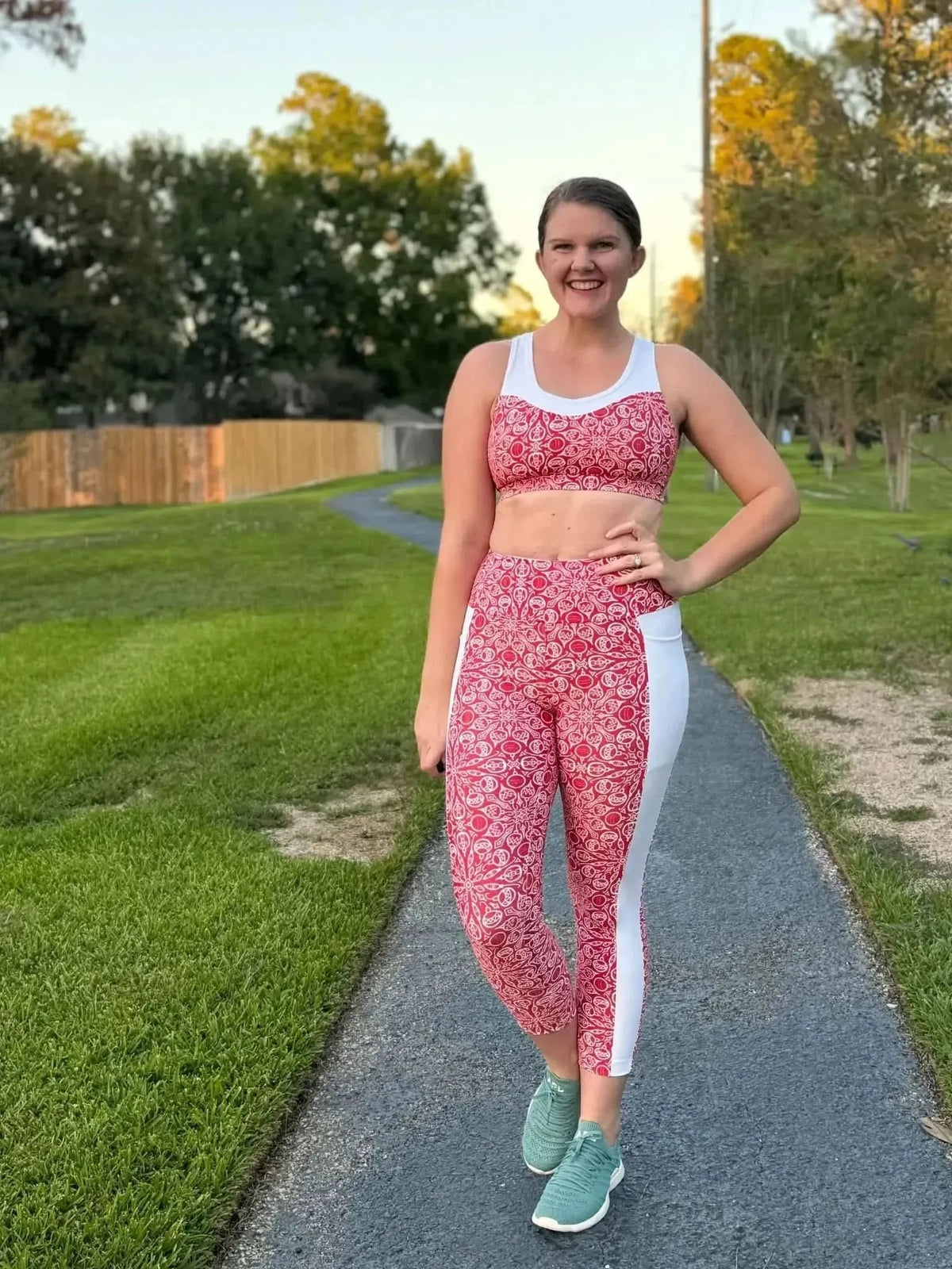 Woman modeling red Christmas holiday print athletic leggings and sports bra on a path.