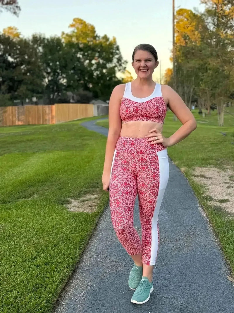 Woman modeling red Christmas holiday print athletic leggings and sports bra on a path.