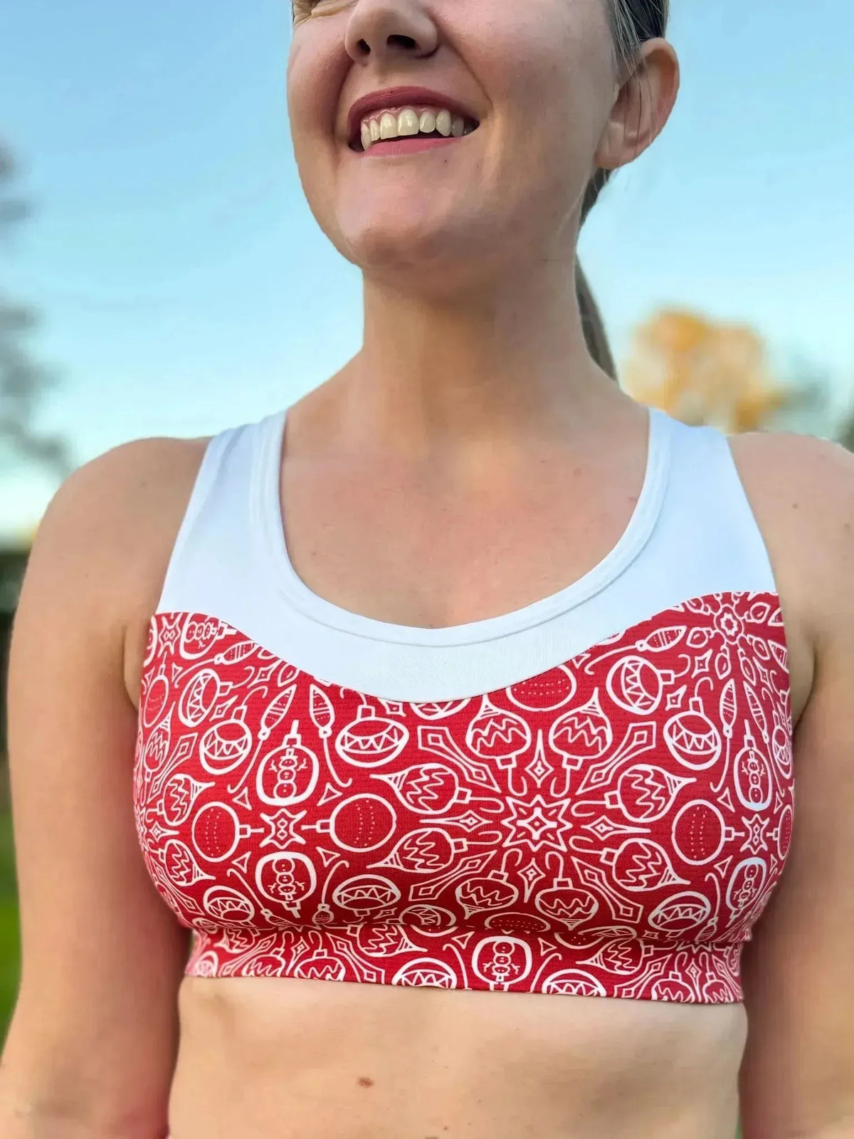 A woman smiles wearing a red and white Christmas holiday print sports bra.
