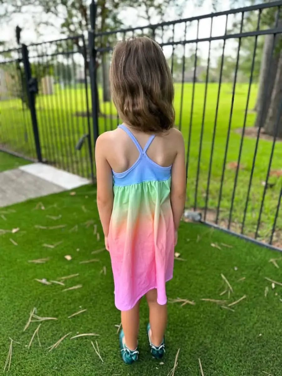 A young girl from behind wears a blue, green, orange, and pink ombre dress.