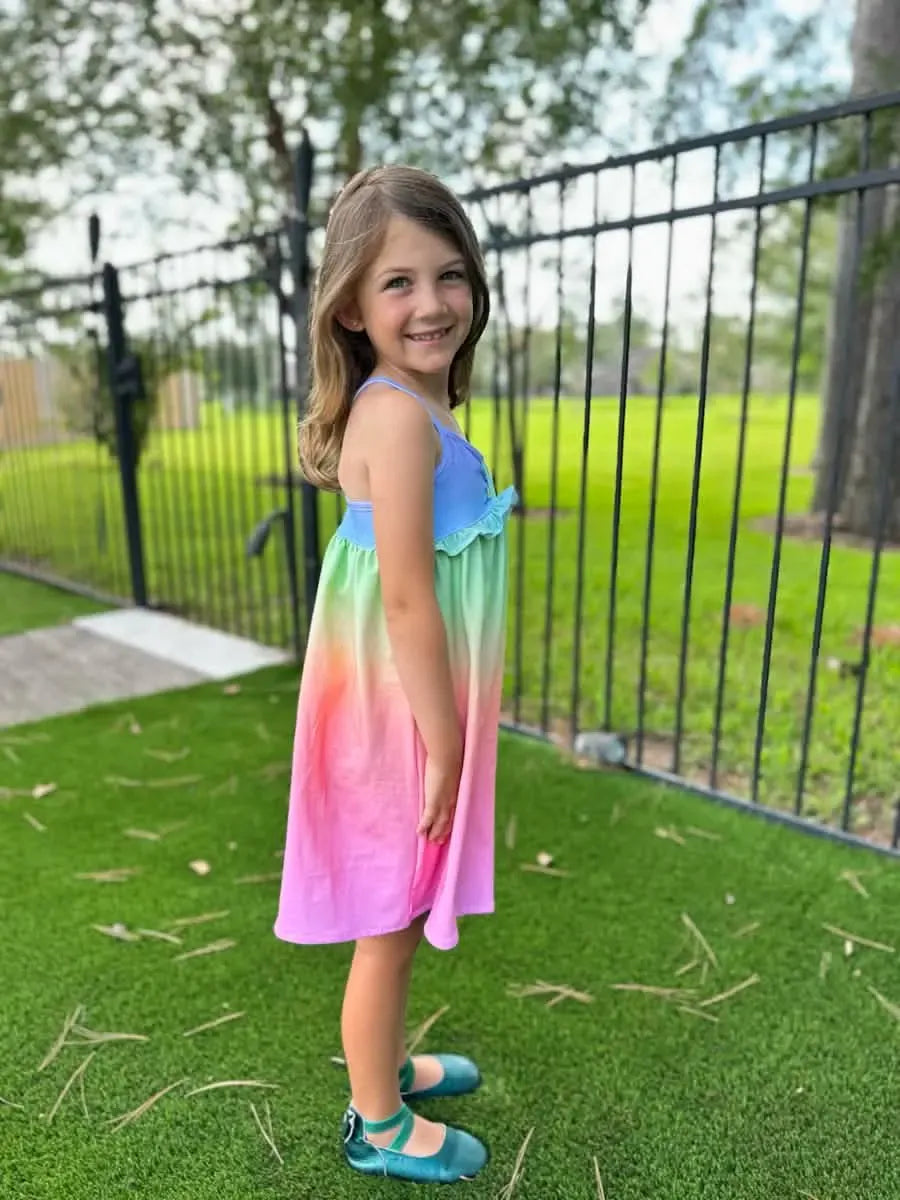 A young girl wears a colorful ombre dress with blue, green, and pink hues.