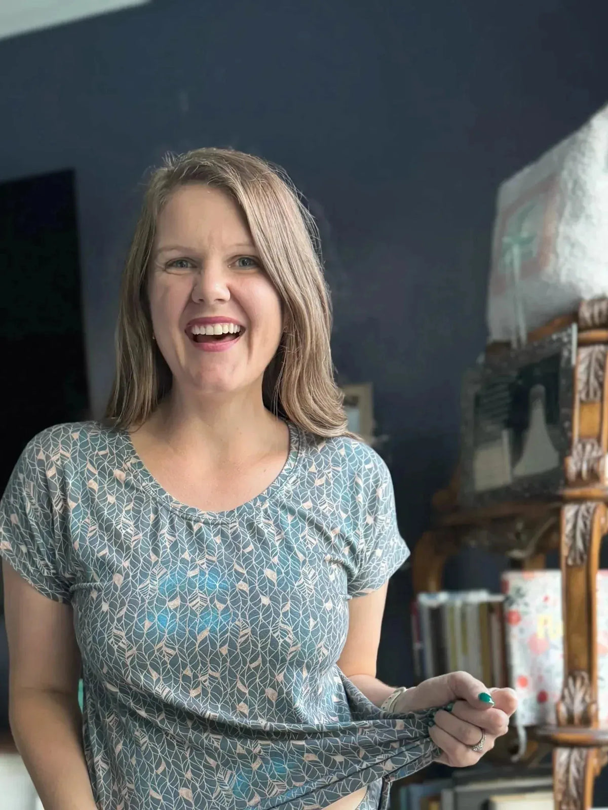 A woman smiles, wearing a teal shirt with a white leaf pattern.
