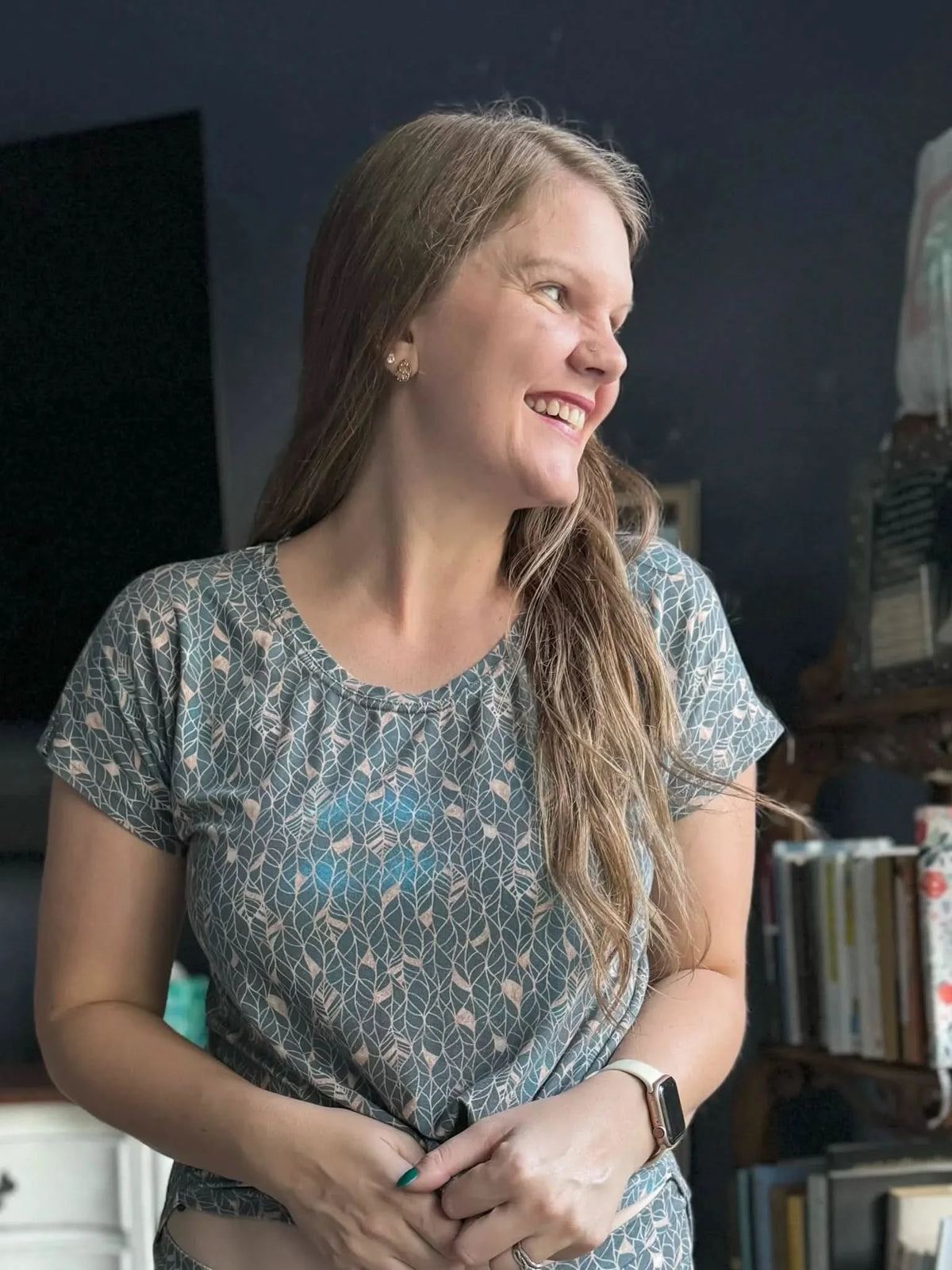 A woman smiles, wearing a teal and tan leaf-patterned shirt.