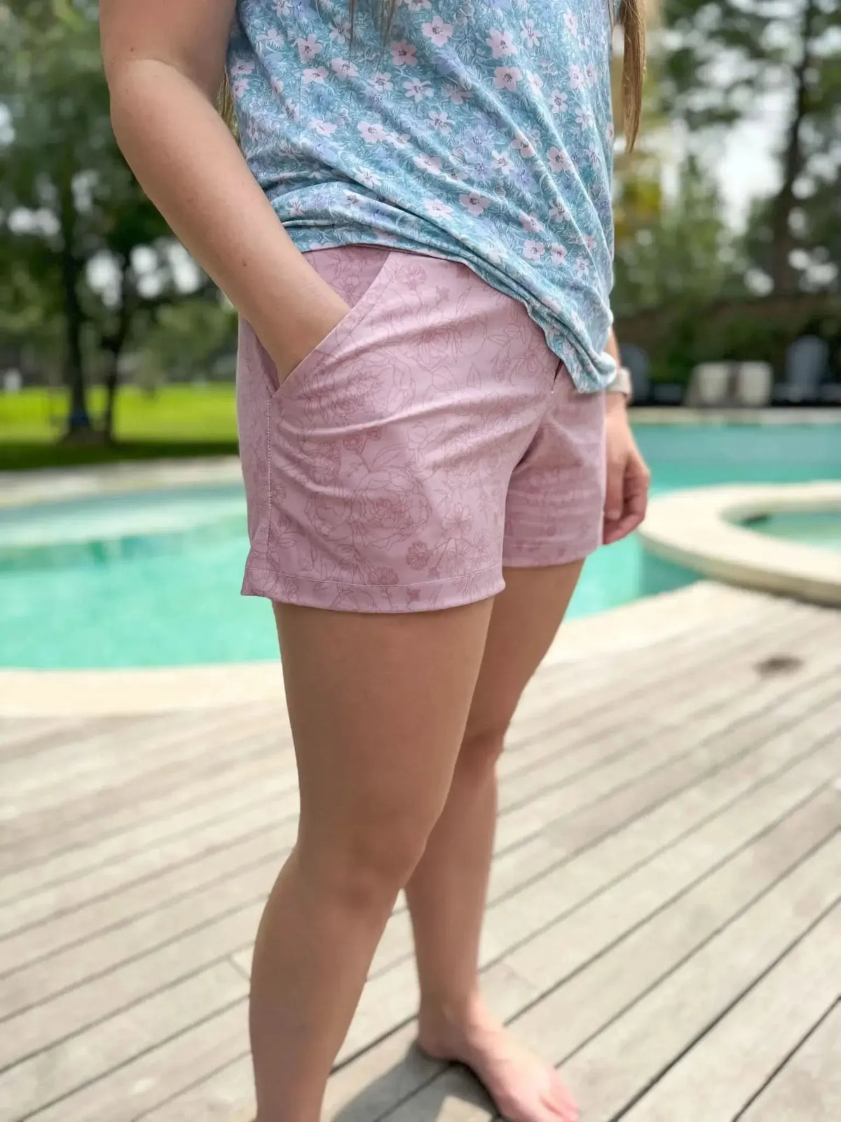 A person wears mauve shorts with a subtle floral pattern and a blue floral top.