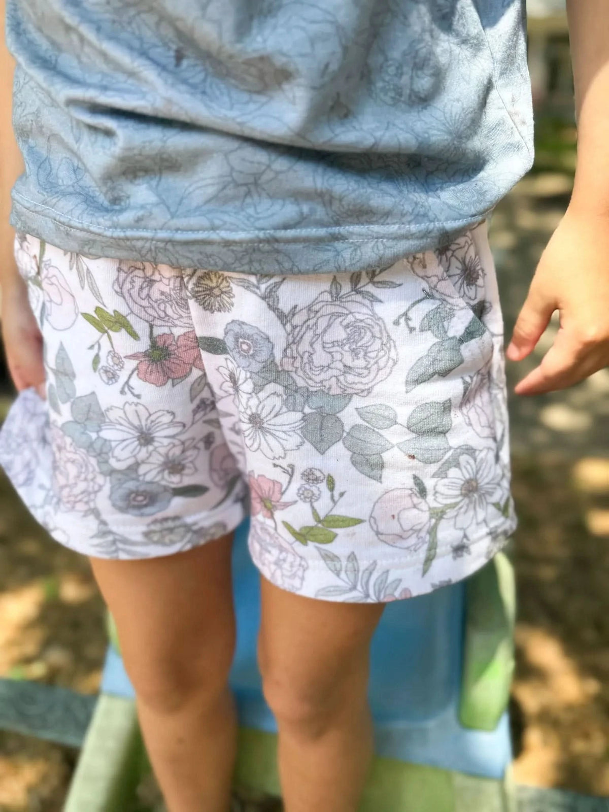 Child wearing floral shorts and a light blue top.