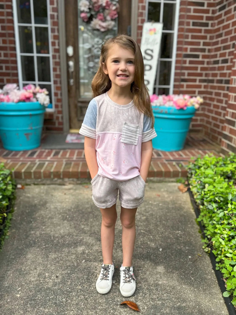 A young girl wears a pink and gray floral top with gray floral shorts.