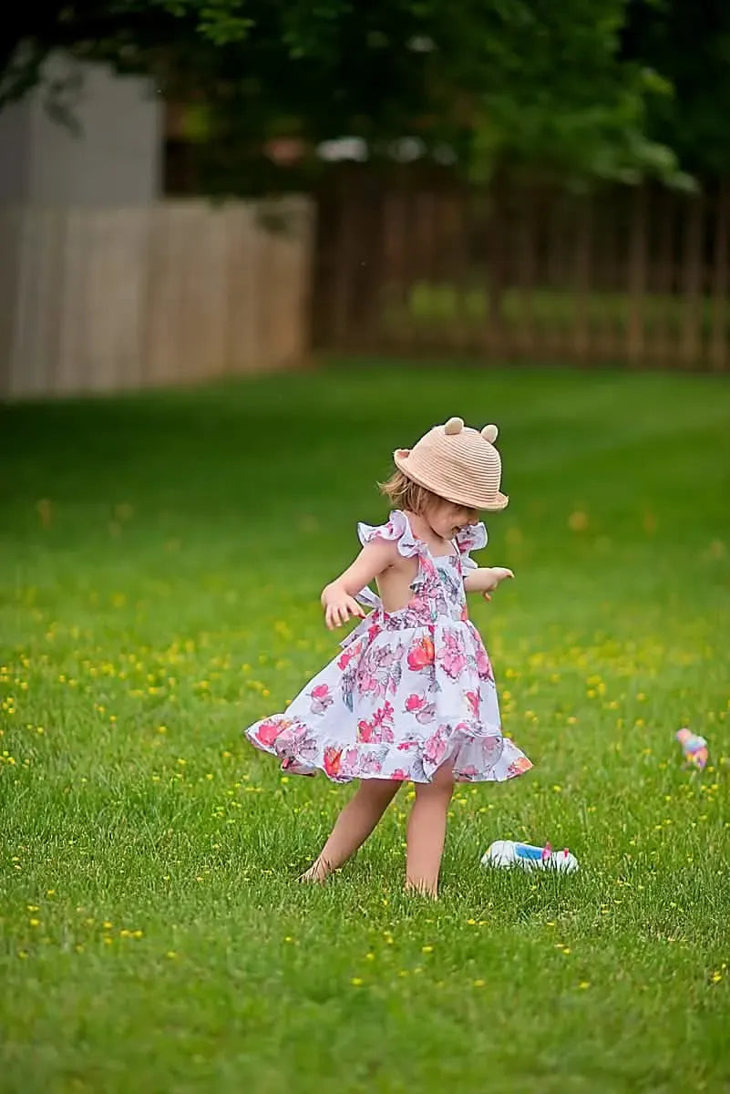 A young child in a floral dress and straw hat plays in a grassy field.