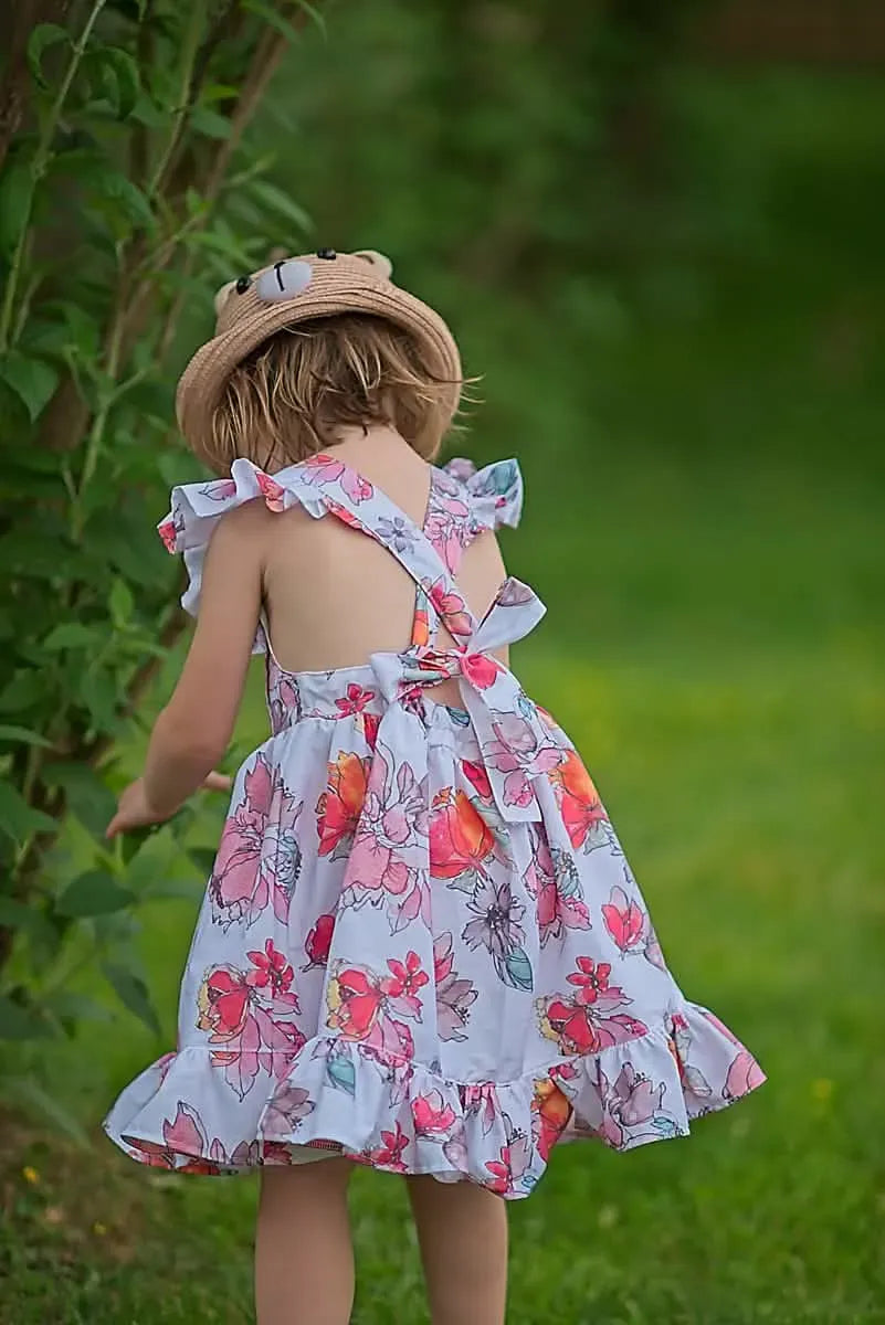 A child in a floral dress and bear hat looks at green leaves.