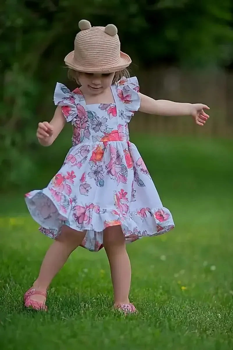 White fabric with tossed floral print in pink and red, shown in a child's dress.