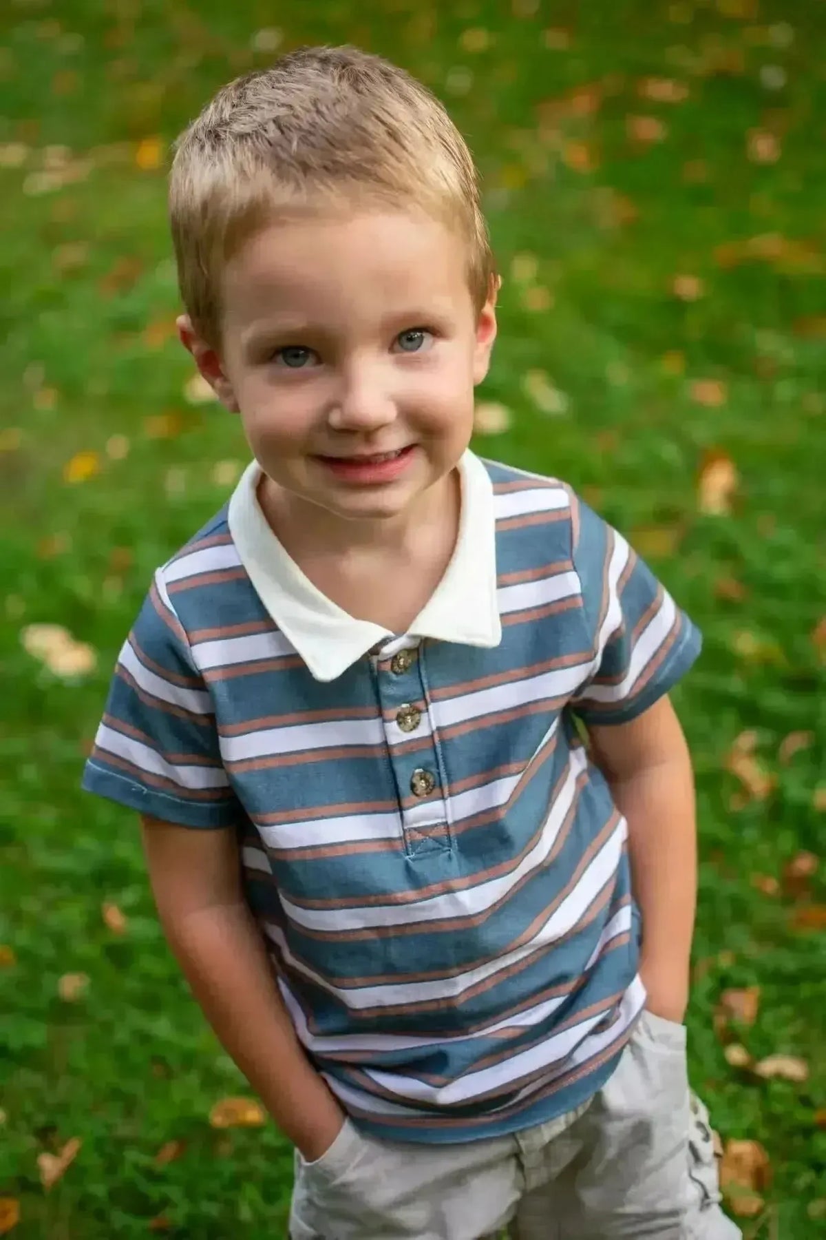 Boy in blue and white striped collared shirt standing on green grass.