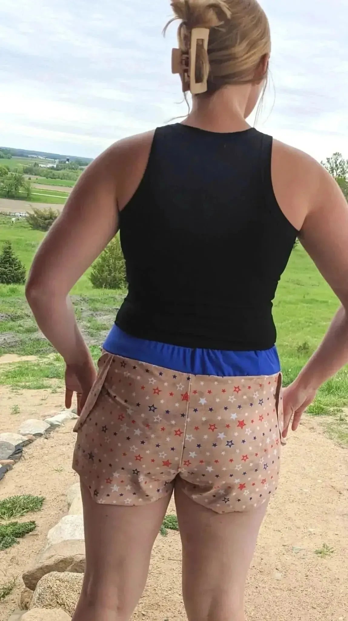 Rear view of woman in black tank top and beige shorts with vintage patriotic star pattern.