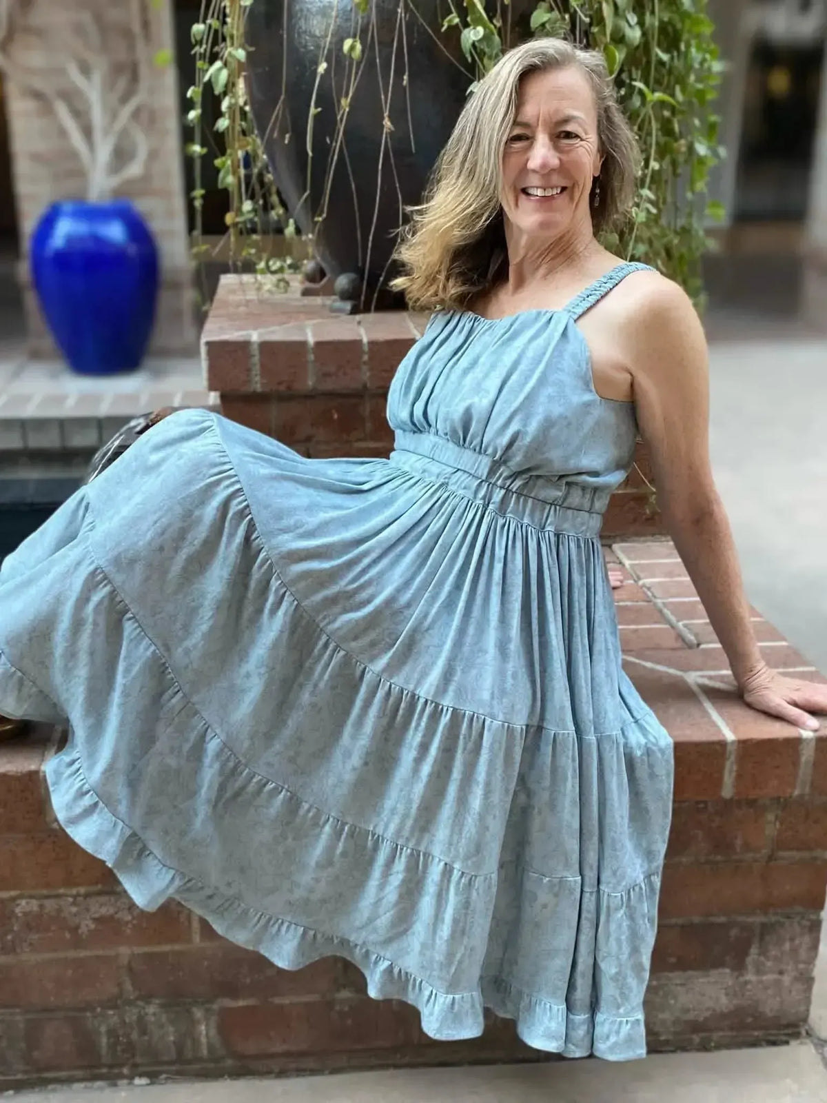 A woman in a dusty blue stenciled floral dress sits on a brick ledge.