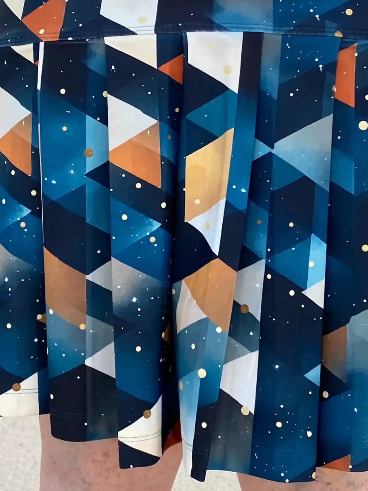 A person wears a pleated skirt with a geometric pattern in blue, white, and orange.