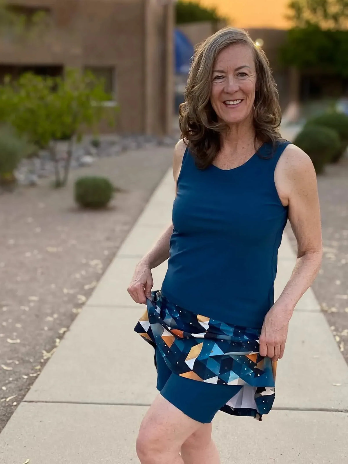 A woman in a teal tank top and a geometric print skirt with shorts underneath.