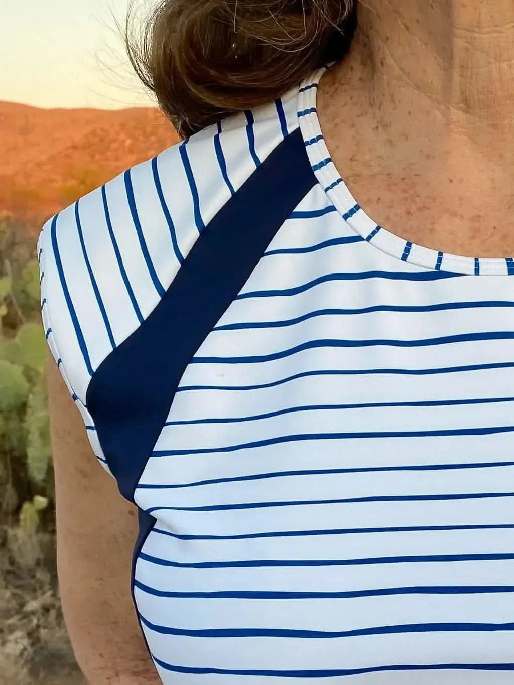 A person wears a white and navy striped top with solid navy shoulder accents.