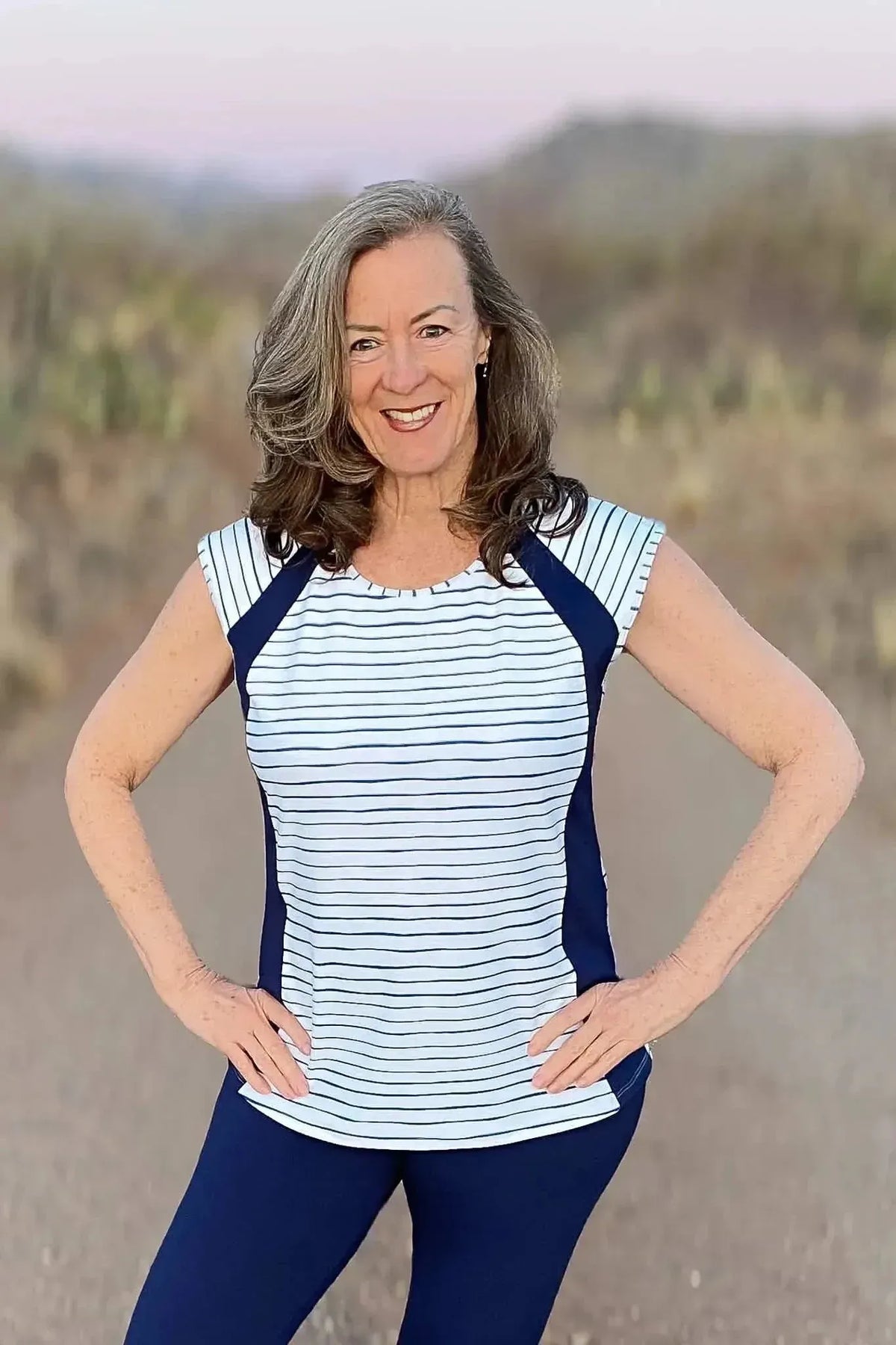 Woman modeling a white striped top with navy accents and pants in a desert landscape.