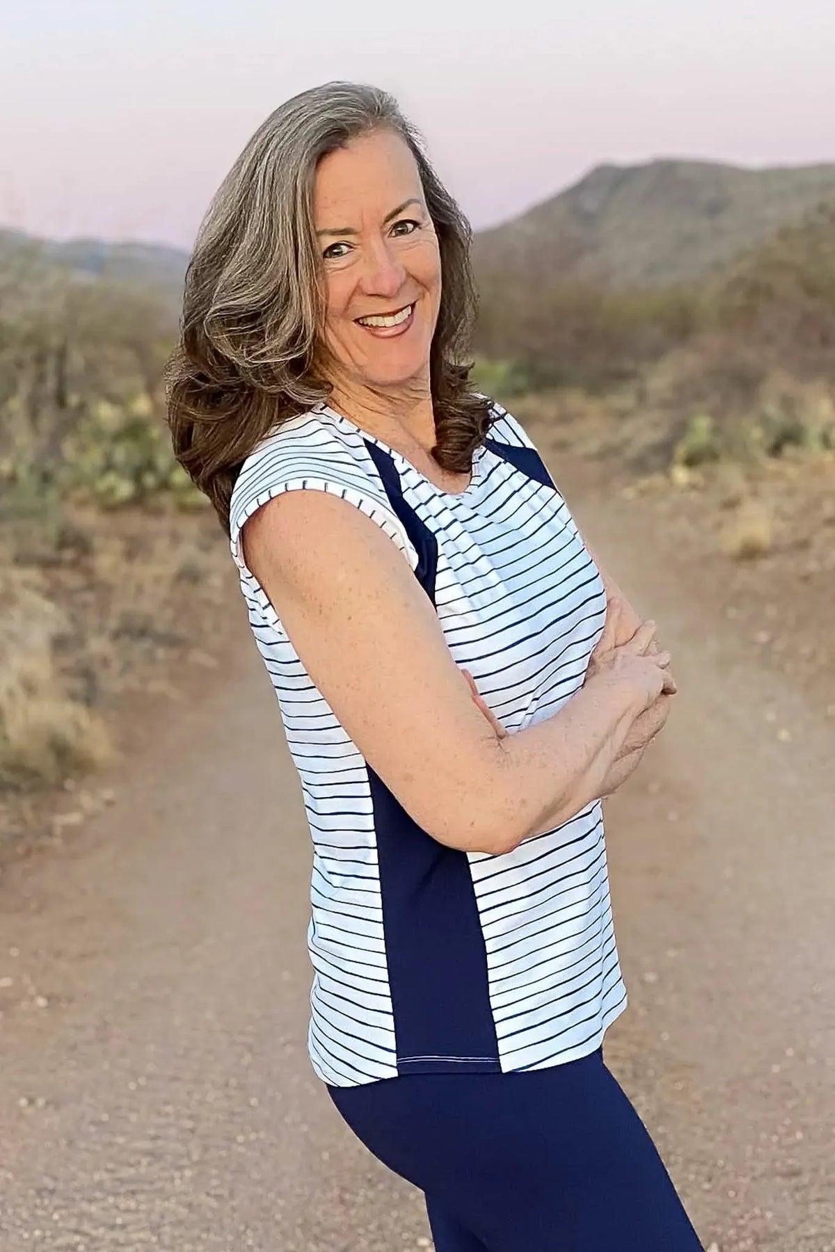 A woman in a navy and white striped top and navy leggings smiles outdoors.