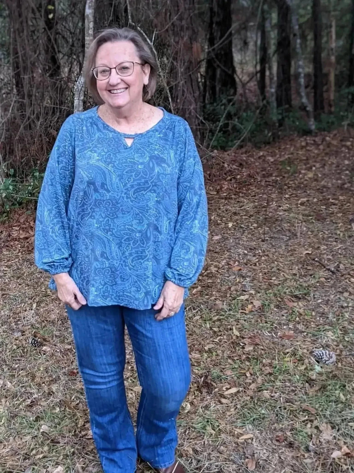 Blue paisley maze patterned fabric sewn into a long-sleeved blouse worn with jeans in a forest.