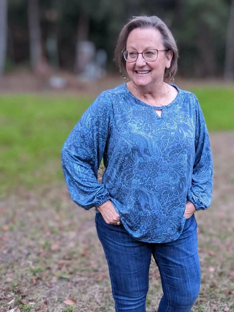 Woman wearing a blue paisley long-sleeved top and jeans.