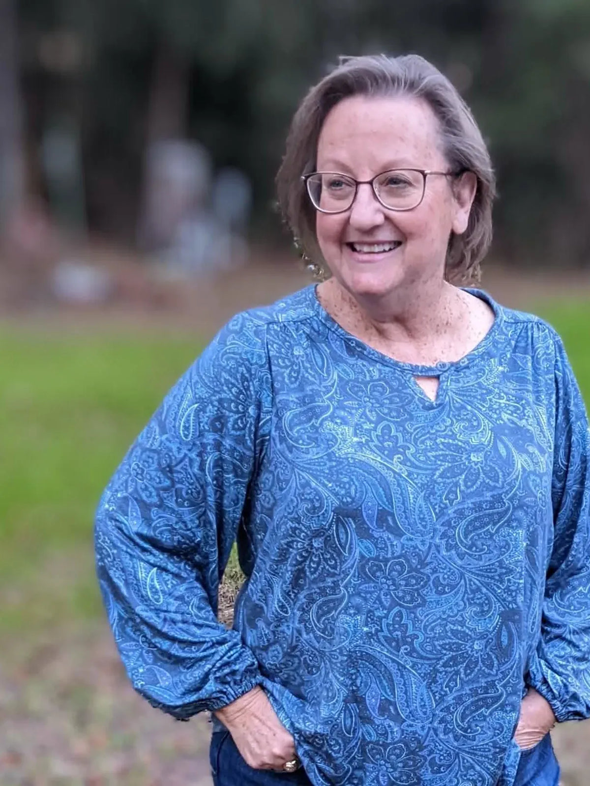 A woman wears a blue paisley maze print top with a keyhole neckline.