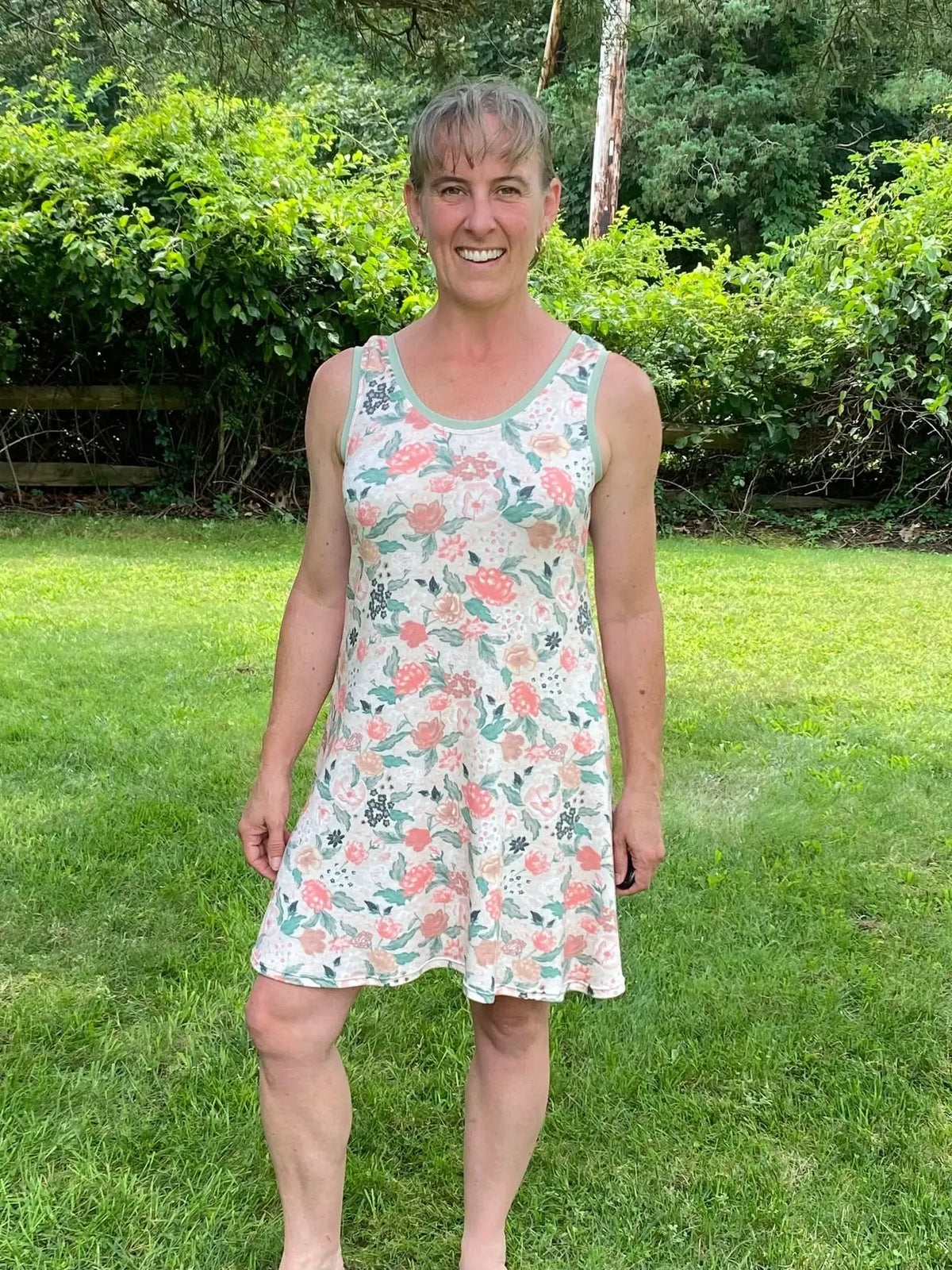 A woman in a floral print dress stands in a grassy yard.