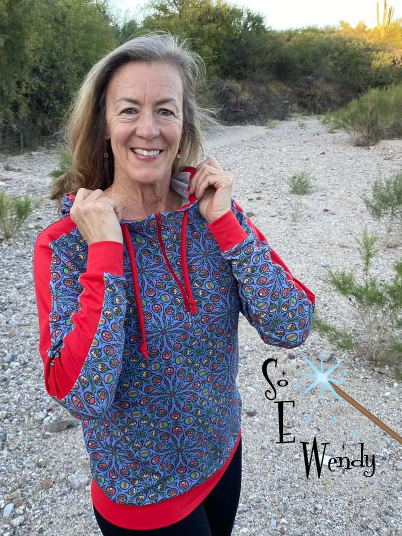 A woman smiles wearing a blue and red patterned Ugly Christmas Sweater.