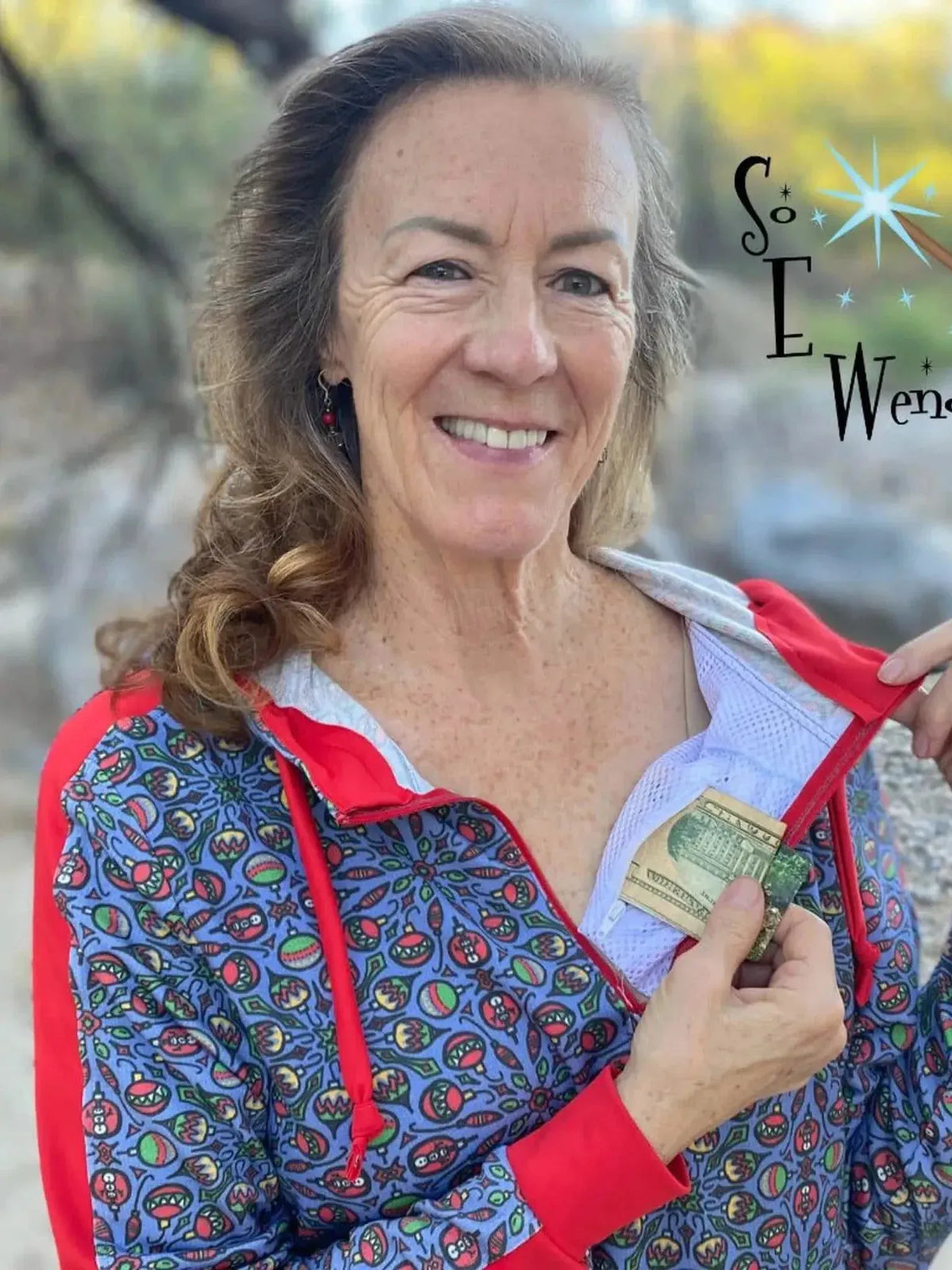 Woman modeling a blue zip-up hoodie with red trim and holiday print, showing a hidden pocket with cash.