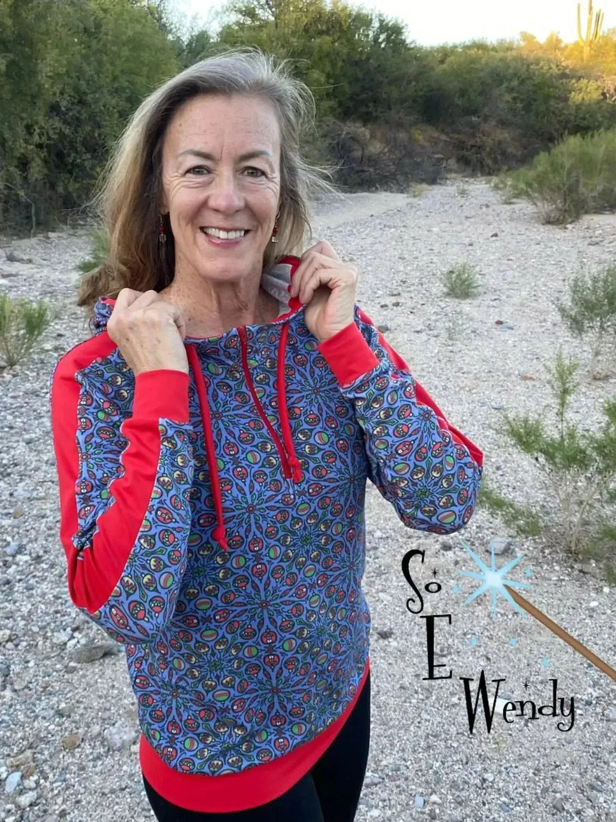 Woman modeling a blue hoodie with red accents and floral print on a desert path.