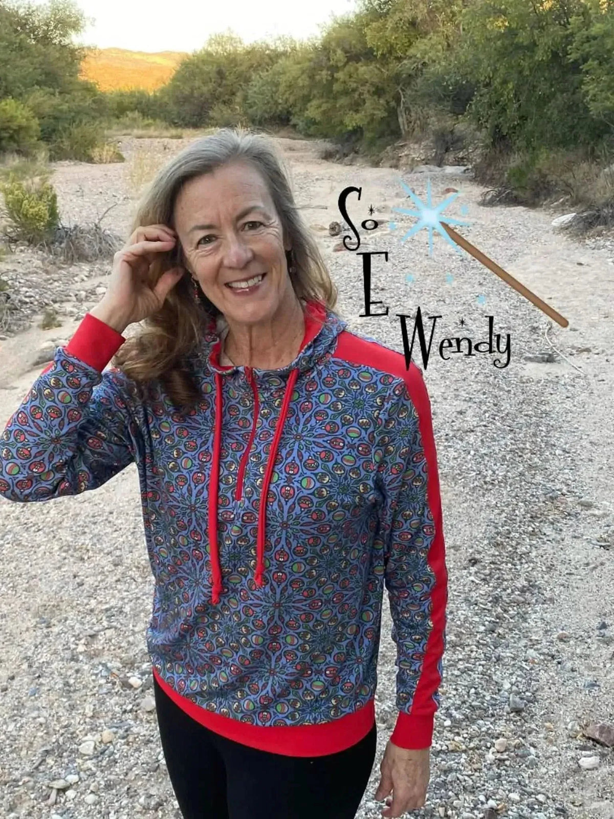 Woman modeling a navy blue floral print hoodie with red trim on a desert trail.