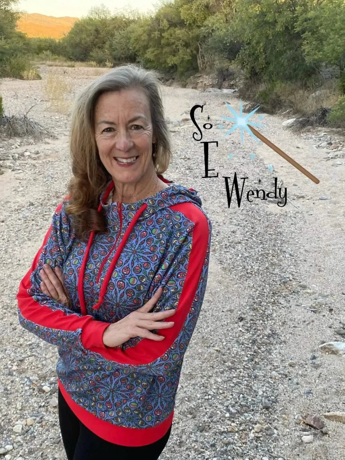 Woman modeling a blue and red patterned hoodie with "So Wendy" text in a desert landscape.